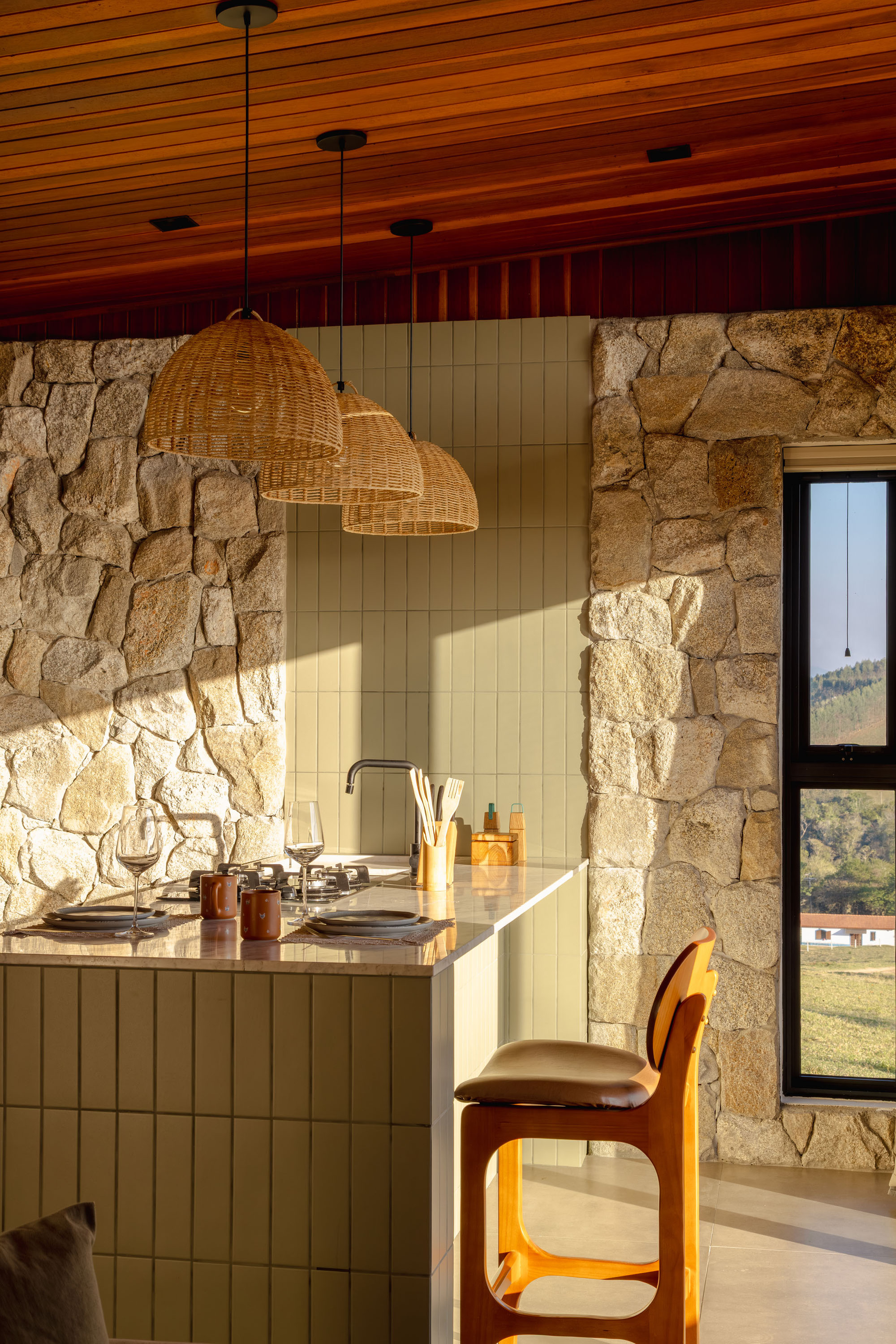 Kitchen counter with woven pendant lights and stone walls under a timber slat ceiling