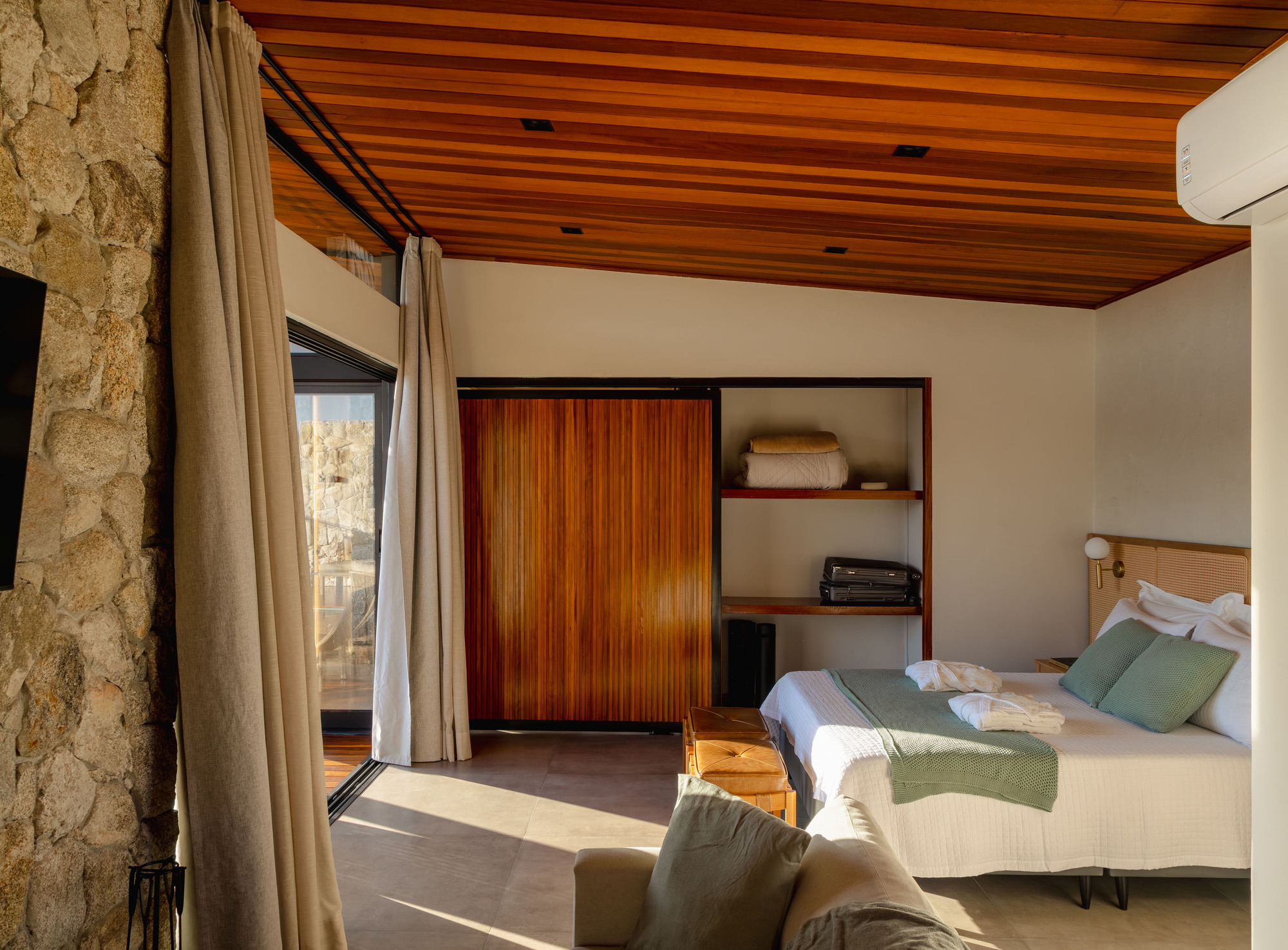 Bedroom with timber slat ceiling and stone column beside floor-to-ceiling curtains in afternoon sunlight