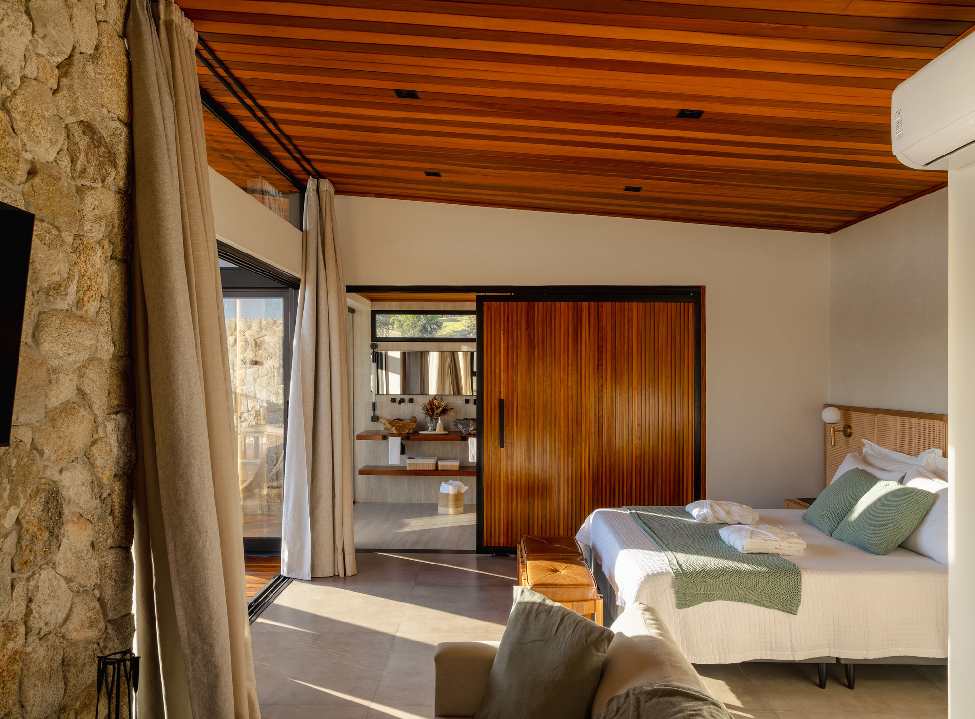 Bedroom view through sliding timber door to ensuite bathroom with stone walls and timber ceiling