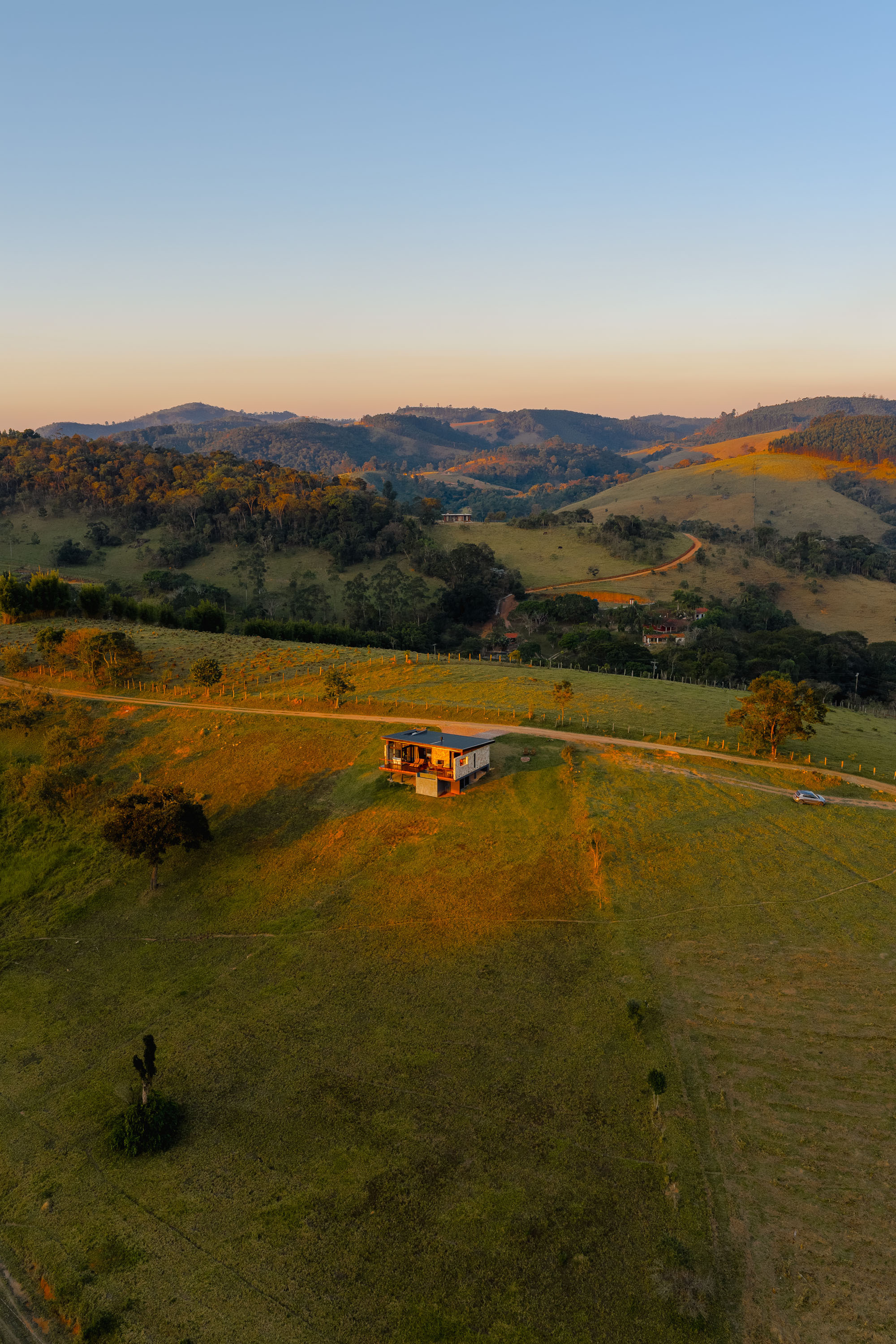 Aerial view of single-story residence in open pasture with rolling hills at sunset