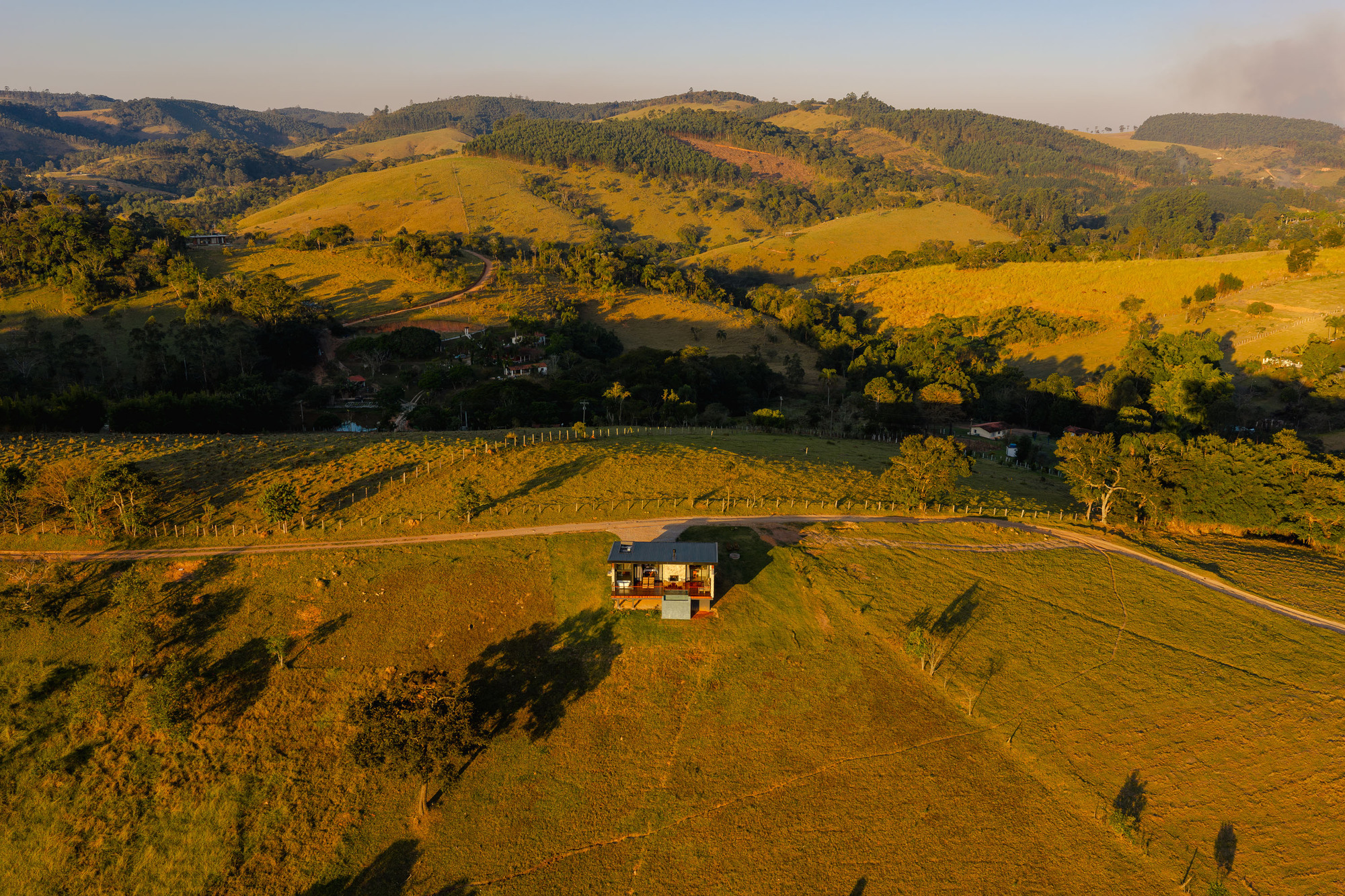 Distant view of the compact house set in vineyard rows with forested hills beyond