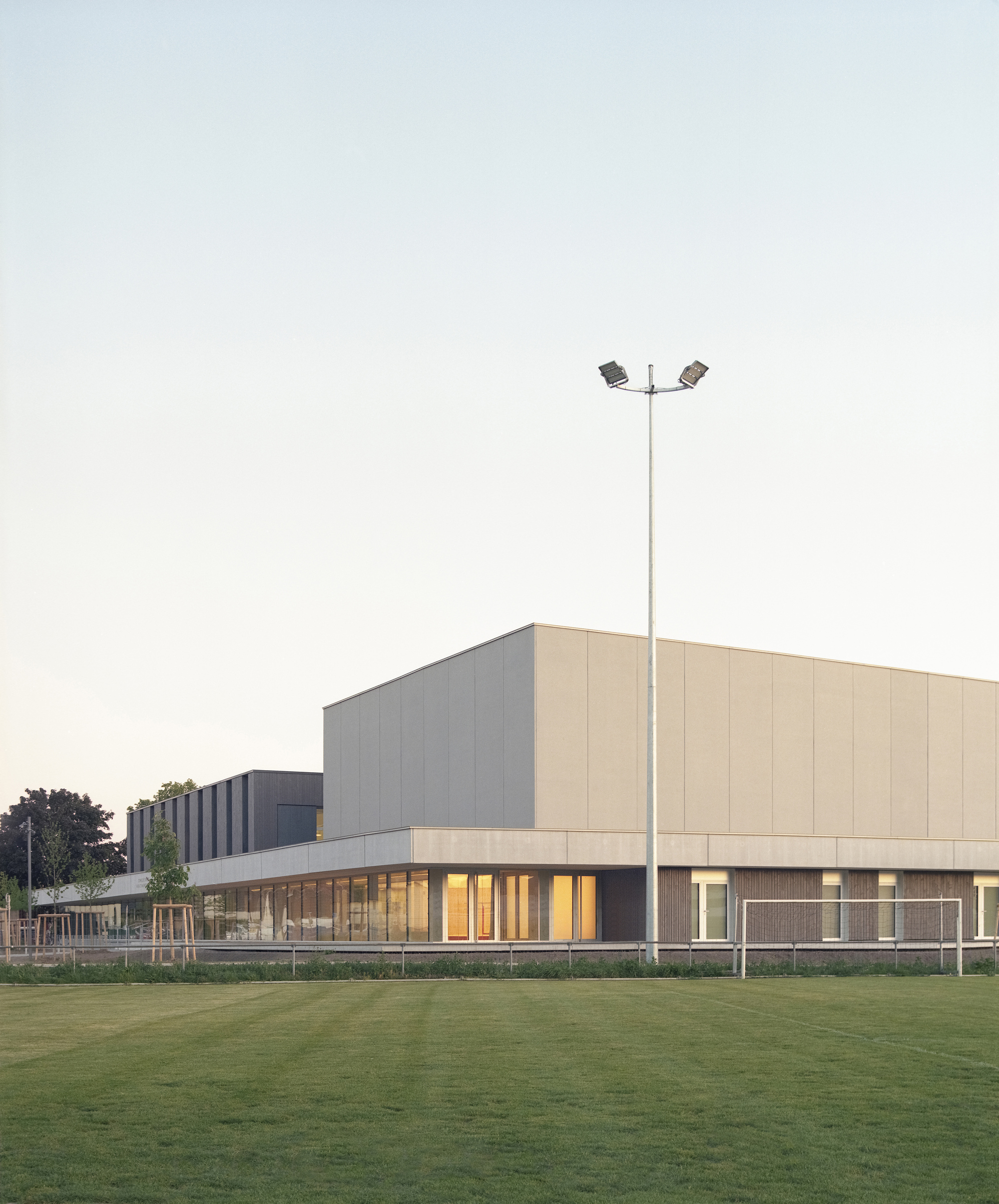 Stacked volumes with vertical ribbed panels and horizontal glazing strip viewed across lawn with light pole