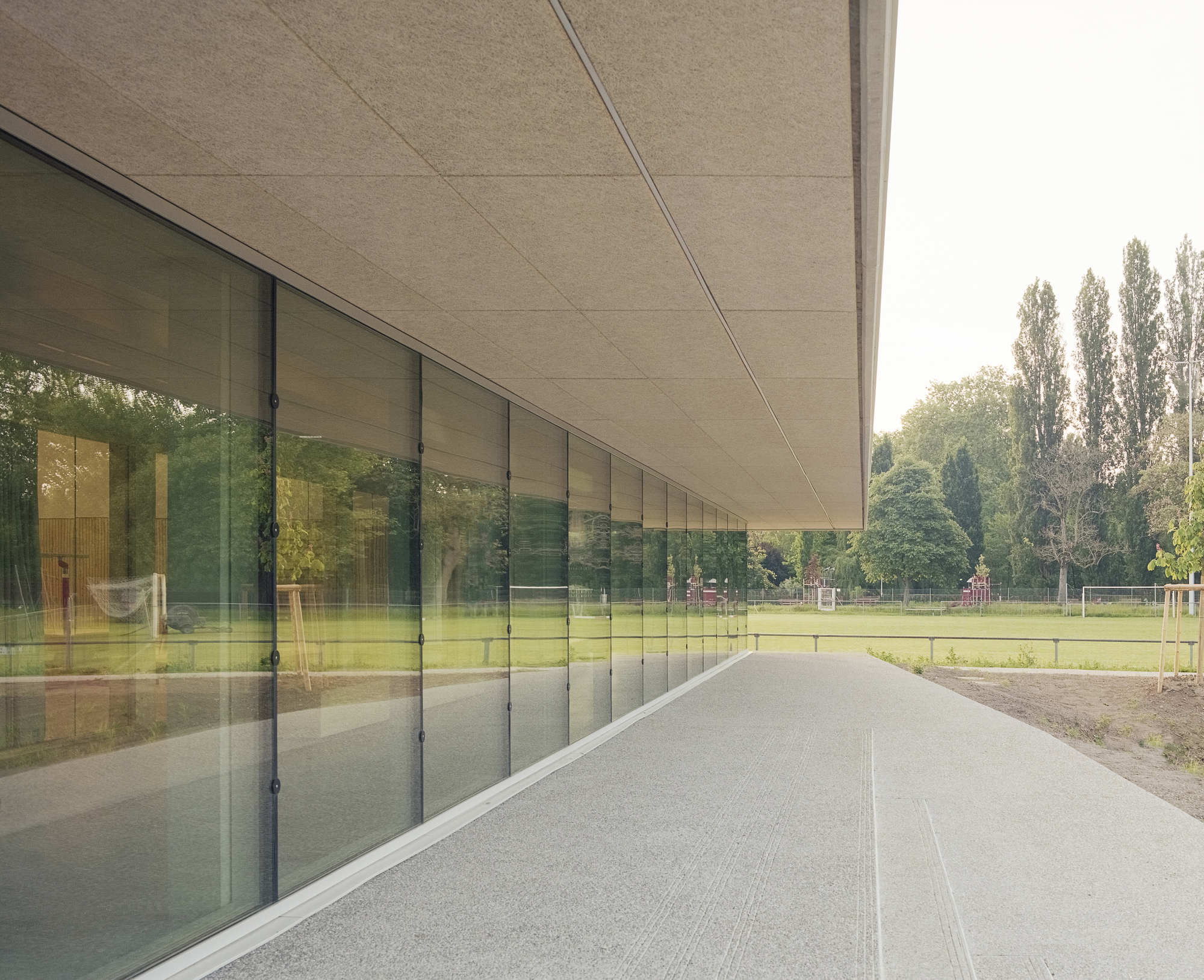 Covered walkway with continuous glazing reflecting sports field and trees beyond under fibrous ceiling panels