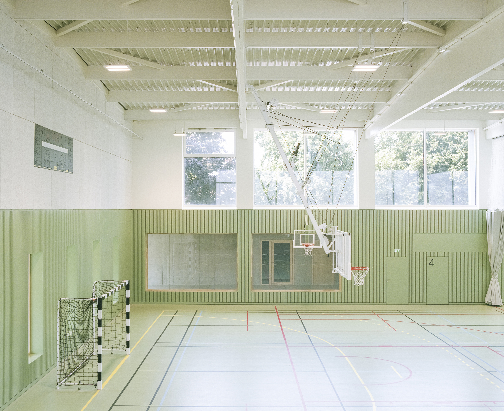 Sports hall with pale green ribbed wall panels and high windows overlooking exterior trees