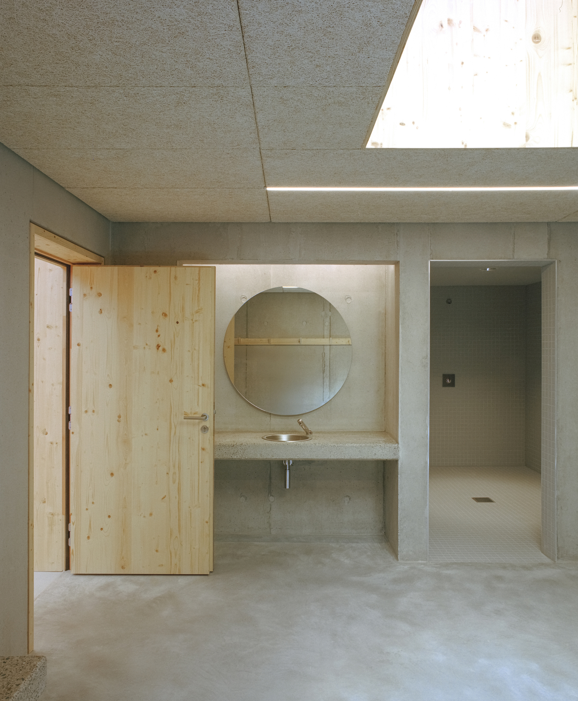 Changing room corridor with concrete sink niche, round mirror and skylight above timber door