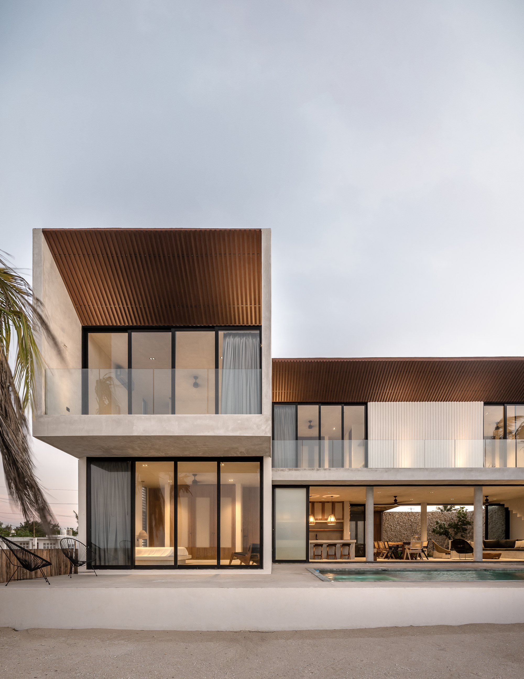Two-story facade with white concrete volumes and ribbed timber soffits at twilight
