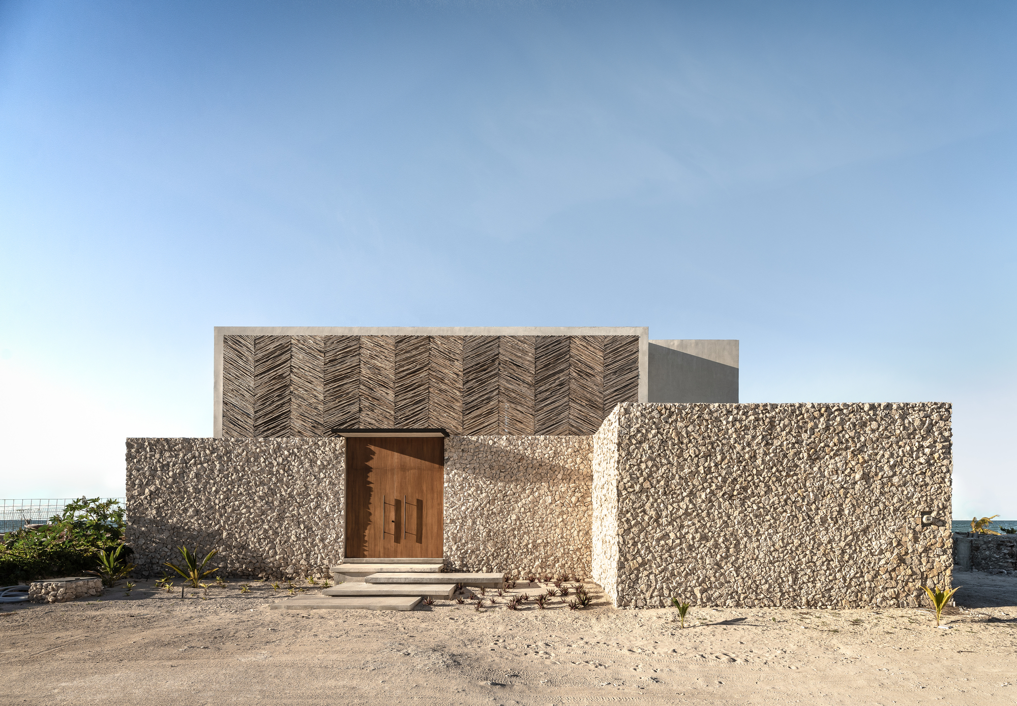 Street view of the facade featuring herringbone timber screens above textured stone walls and a central timber door