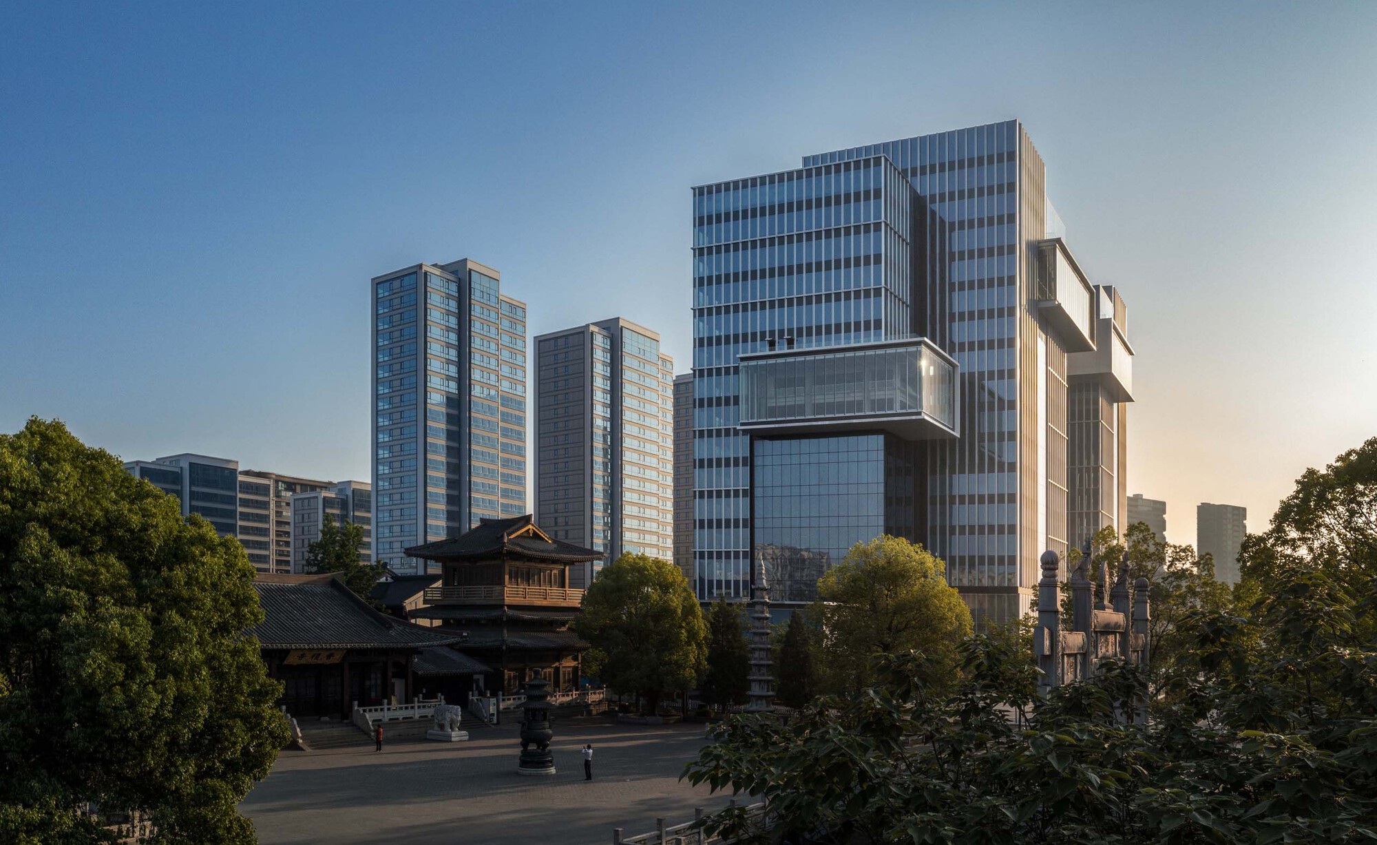 Cluster of glass tower blocks rising beyond a traditional temple structure and surrounding trees