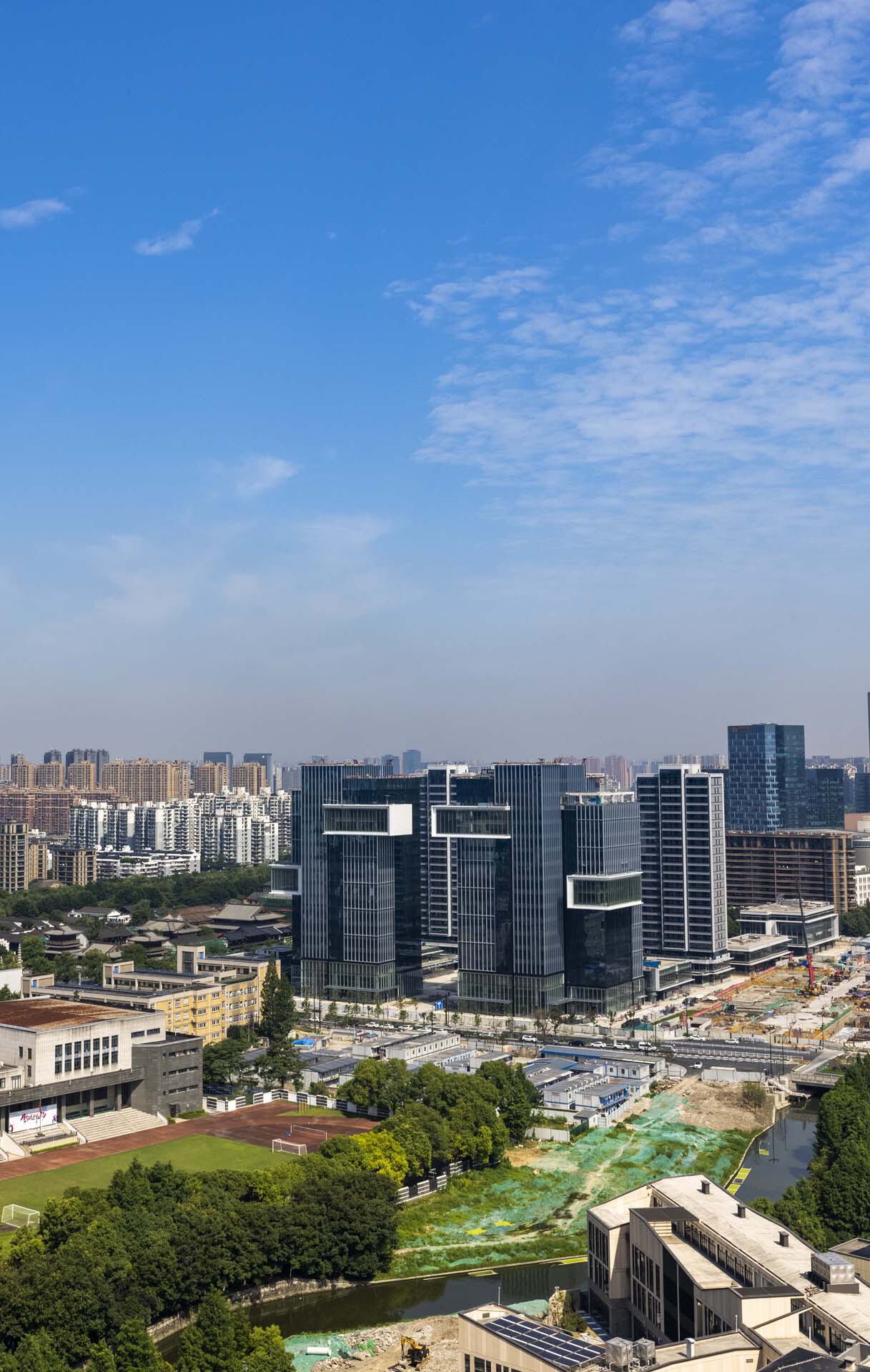 Aerial view of offset glass office towers amid low-rise buildings and a green canal corridor