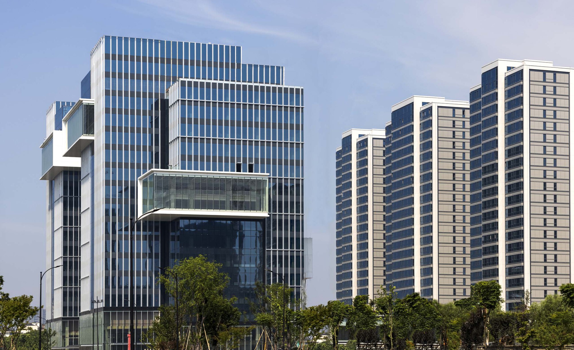 Vertical louvered glass facade with cantilevered volumes beside rows of residential high-rises