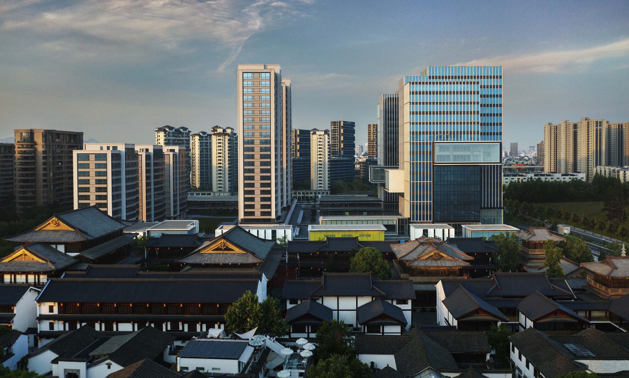 Cluster of stepped glass and concrete towers behind the low-rise traditional timber rooflines at sunset