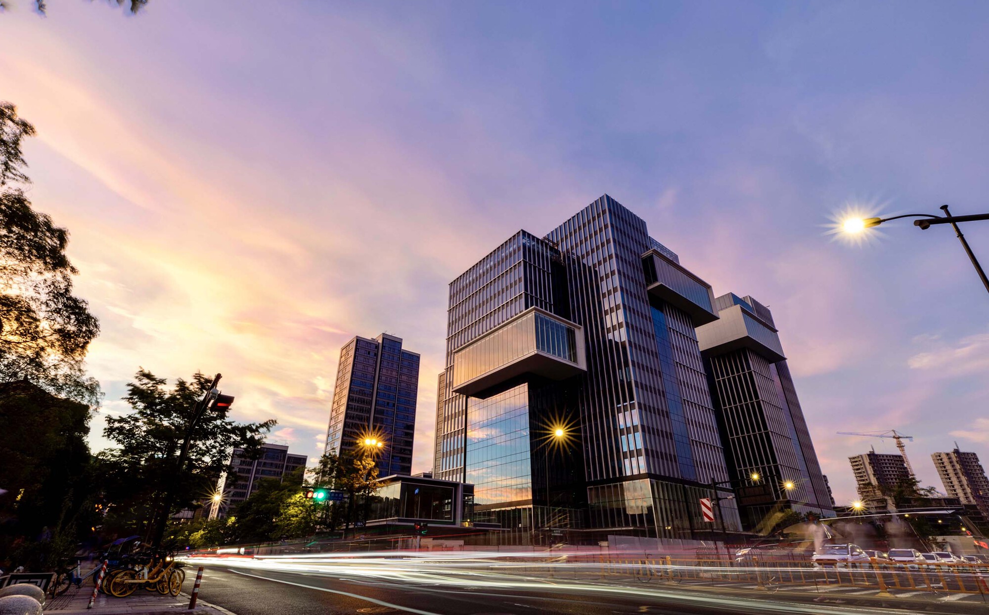 Articulated facade of cantilevered glass and metal volumes above a busy street at dusk