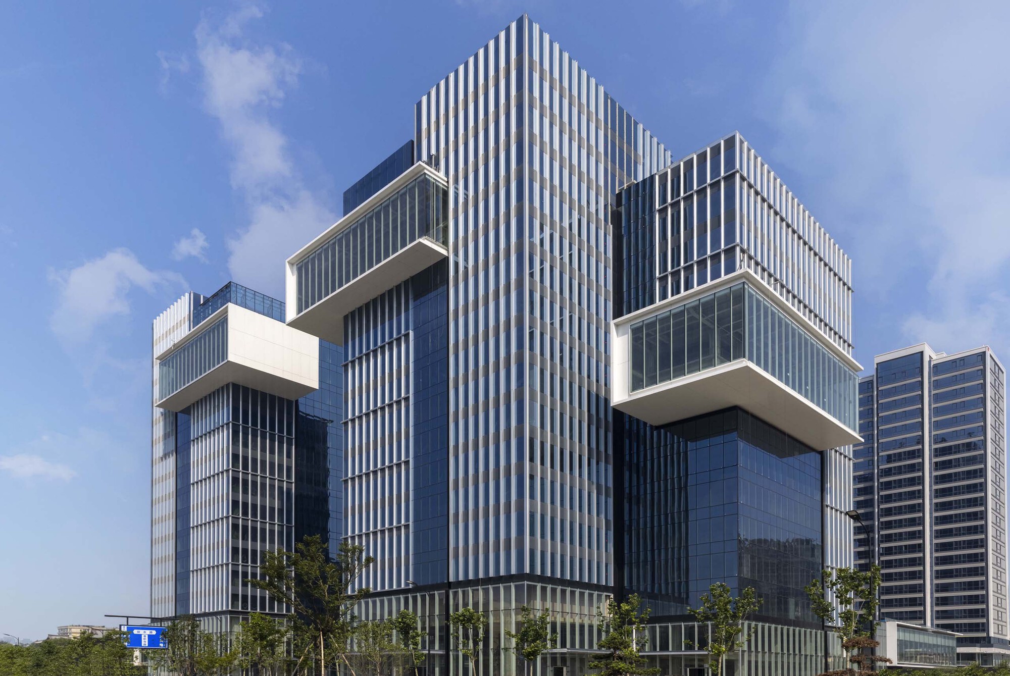 Central tower with vertical ribbed cladding flanked by cantilevered glass volumes under blue sky