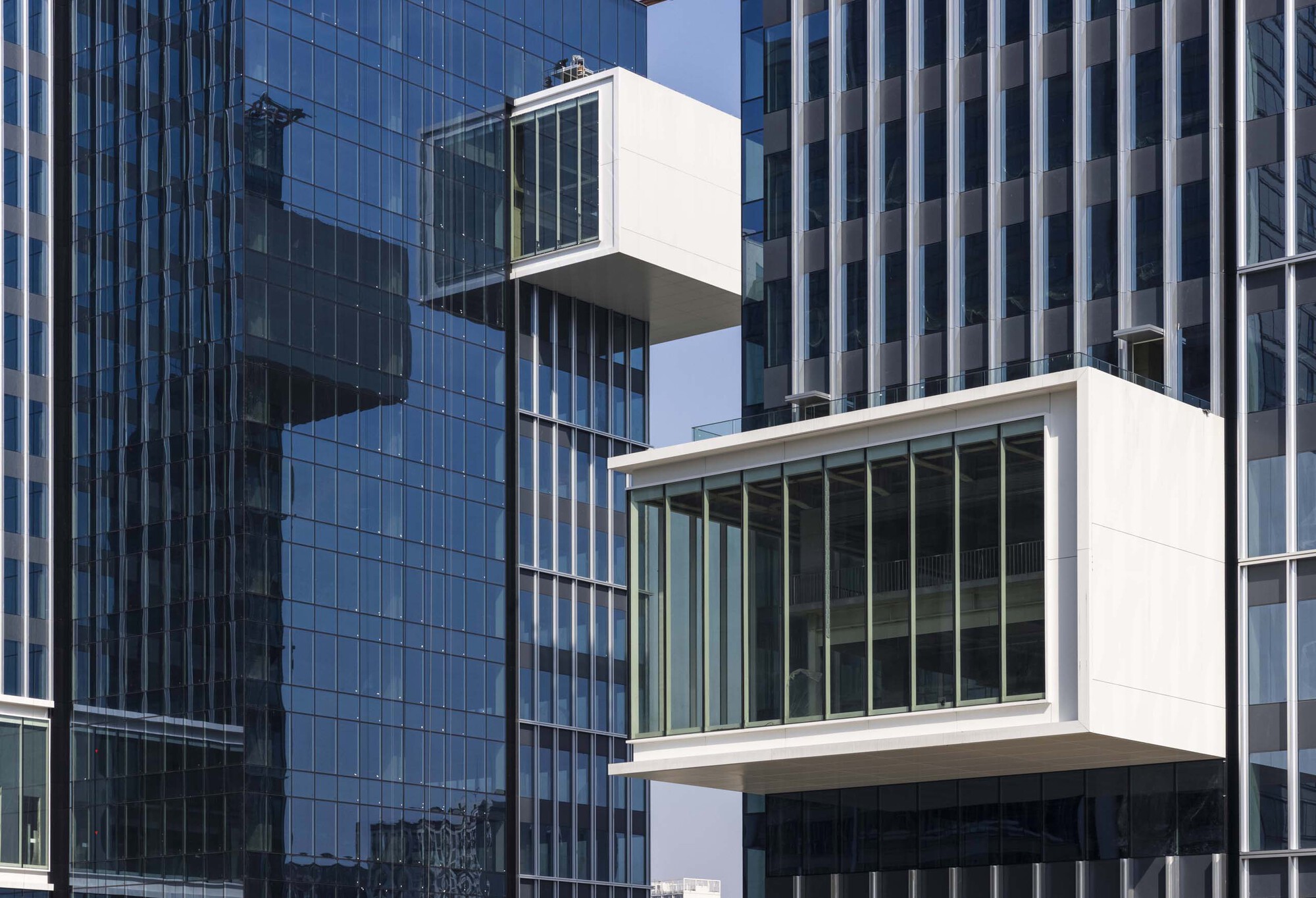 Two stacked white cantilevered glass boxes projecting from a blue glass curtain wall tower