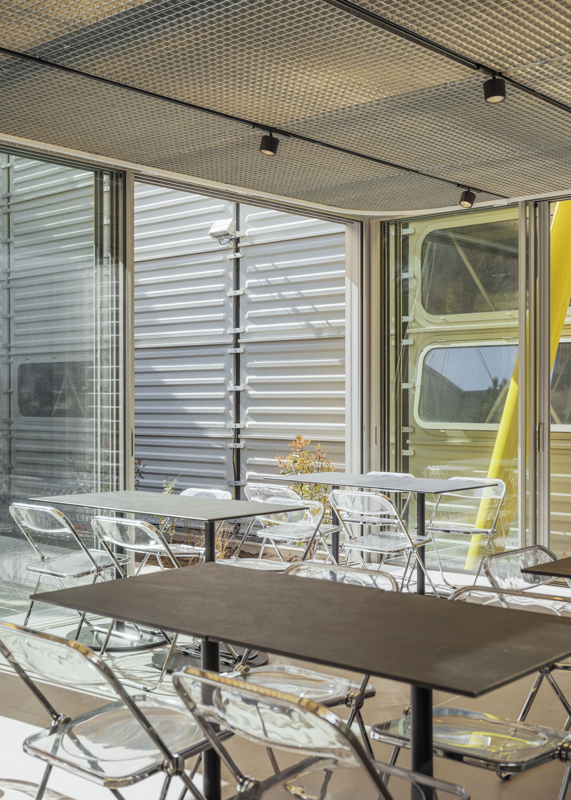 Covered patio with clear acrylic chairs and perforated acoustic ceiling panels beneath retractable awnings