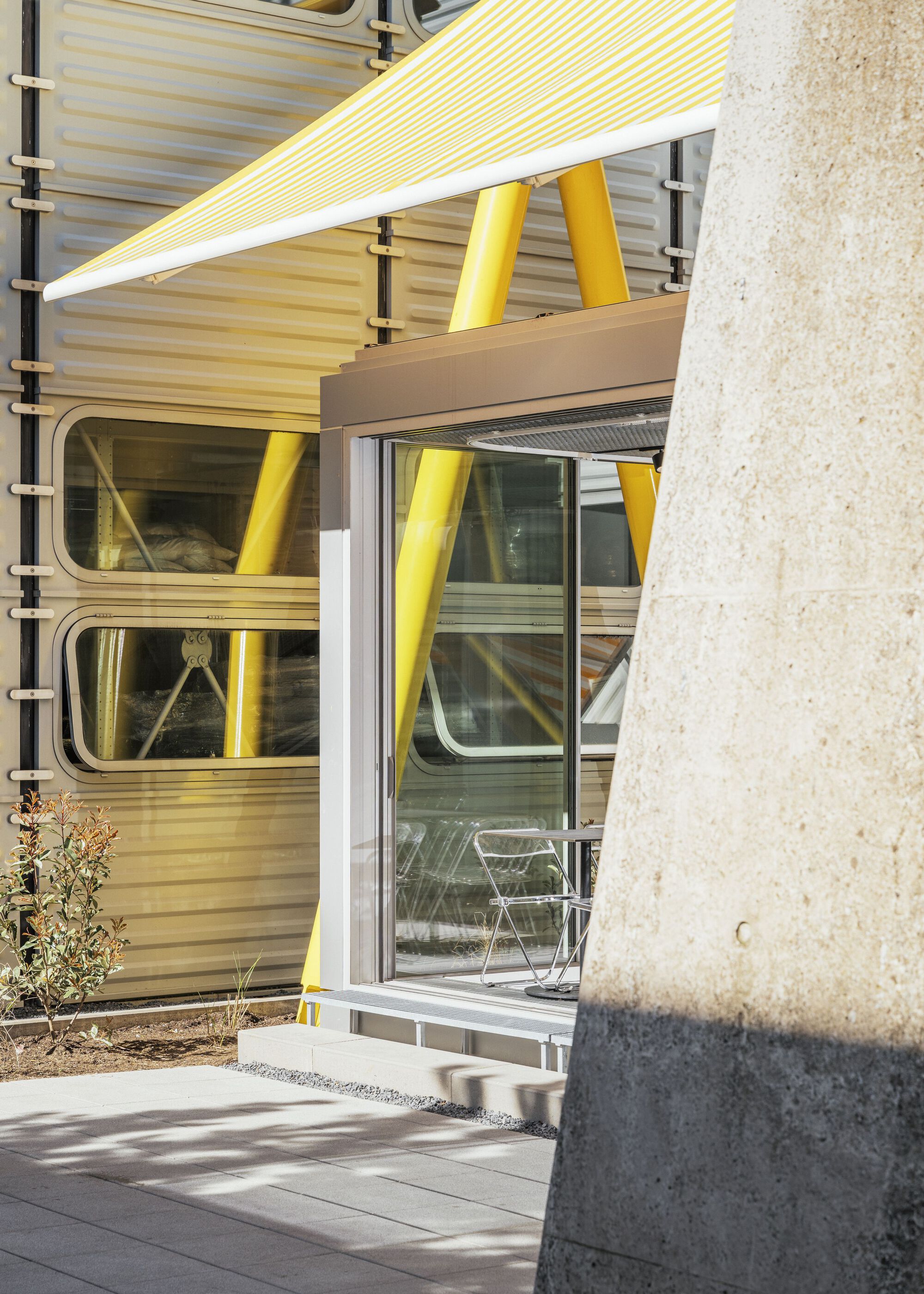 Sliding glass doors beneath yellow canopy with concrete column in foreground casting afternoon shadow