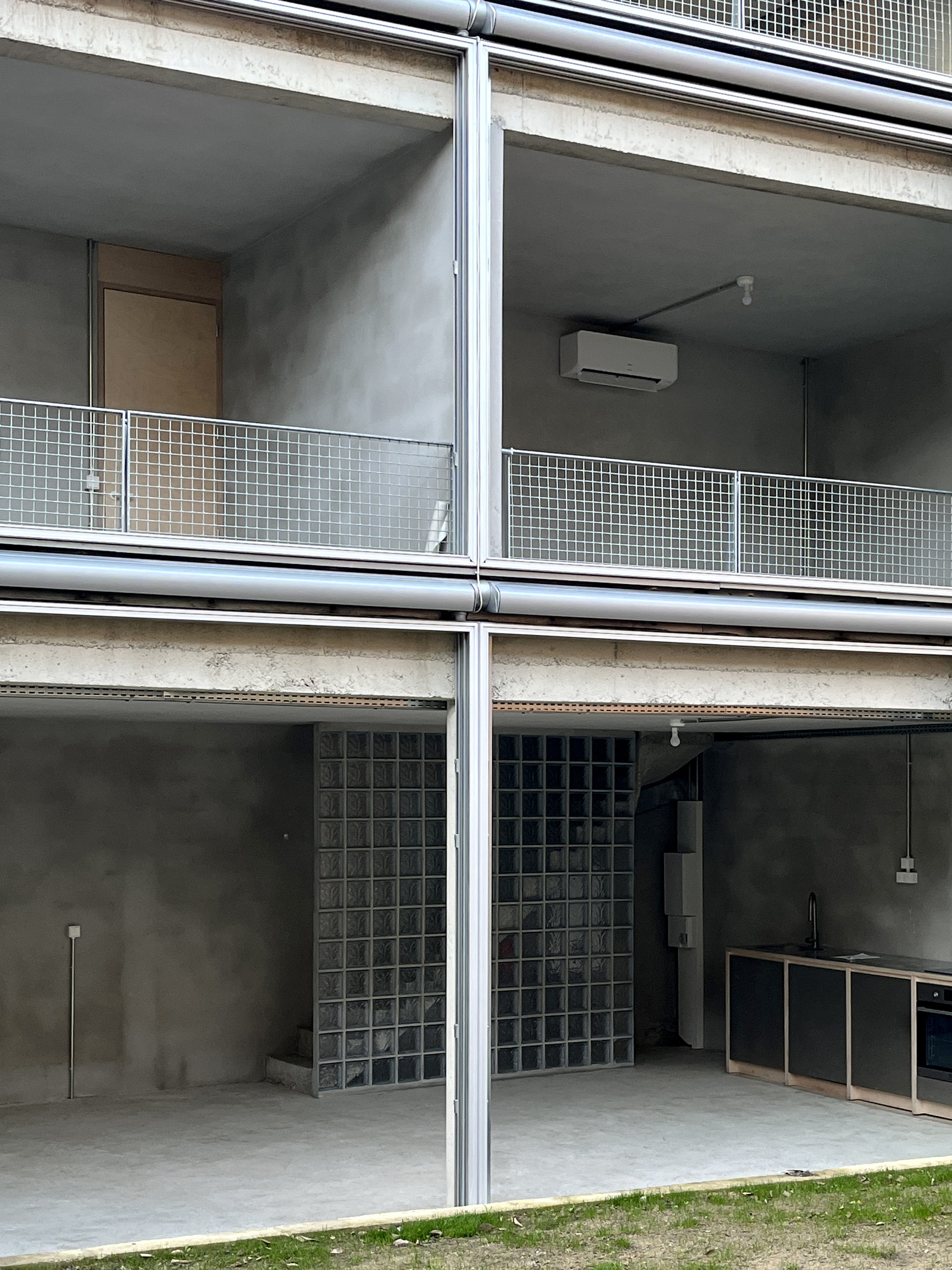 Stacked balconies with glass block walls, metal railings, and concrete soffit under overcast sky