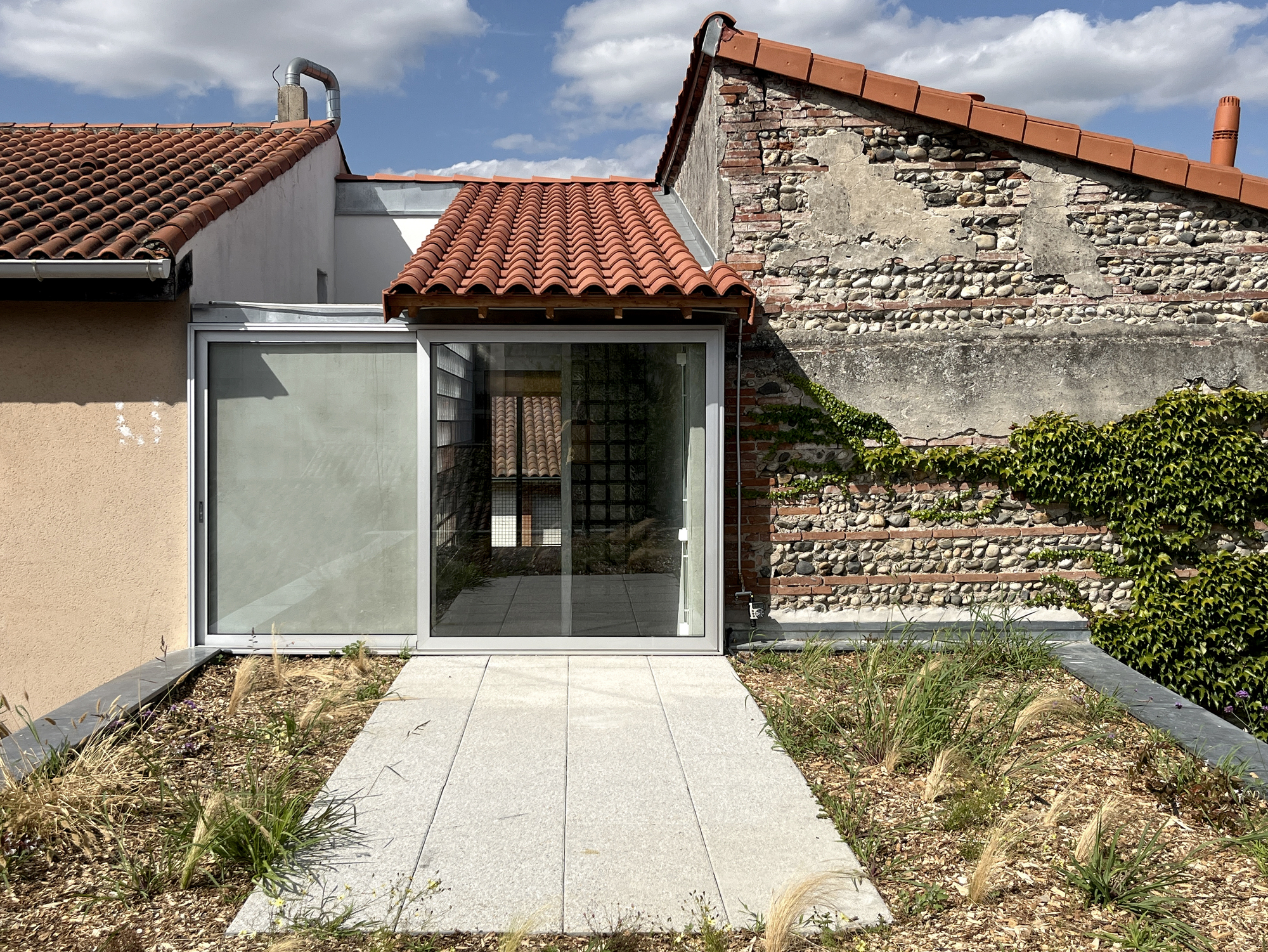 Glass extension with terracotta roof tiles meeting exposed brick wall and gravel courtyard planting