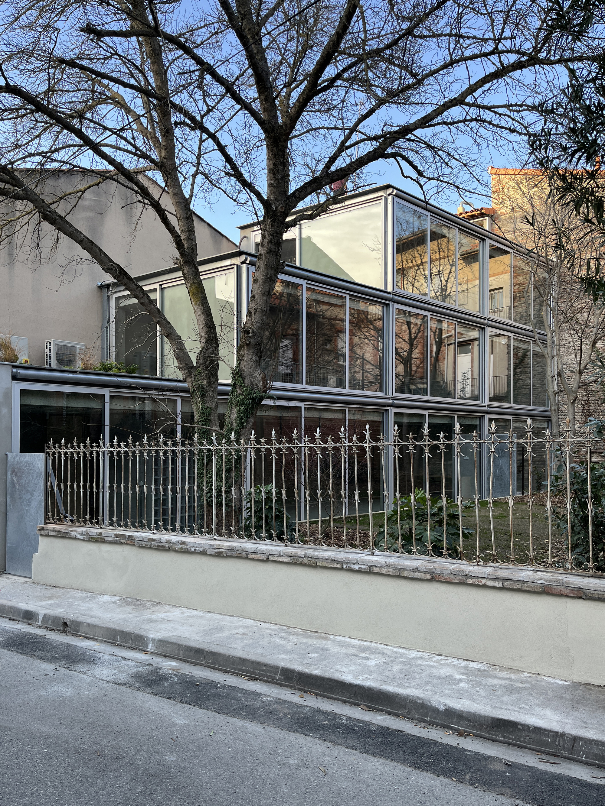 Street view of the white-framed glass extension behind a metal railing and bare winter trees