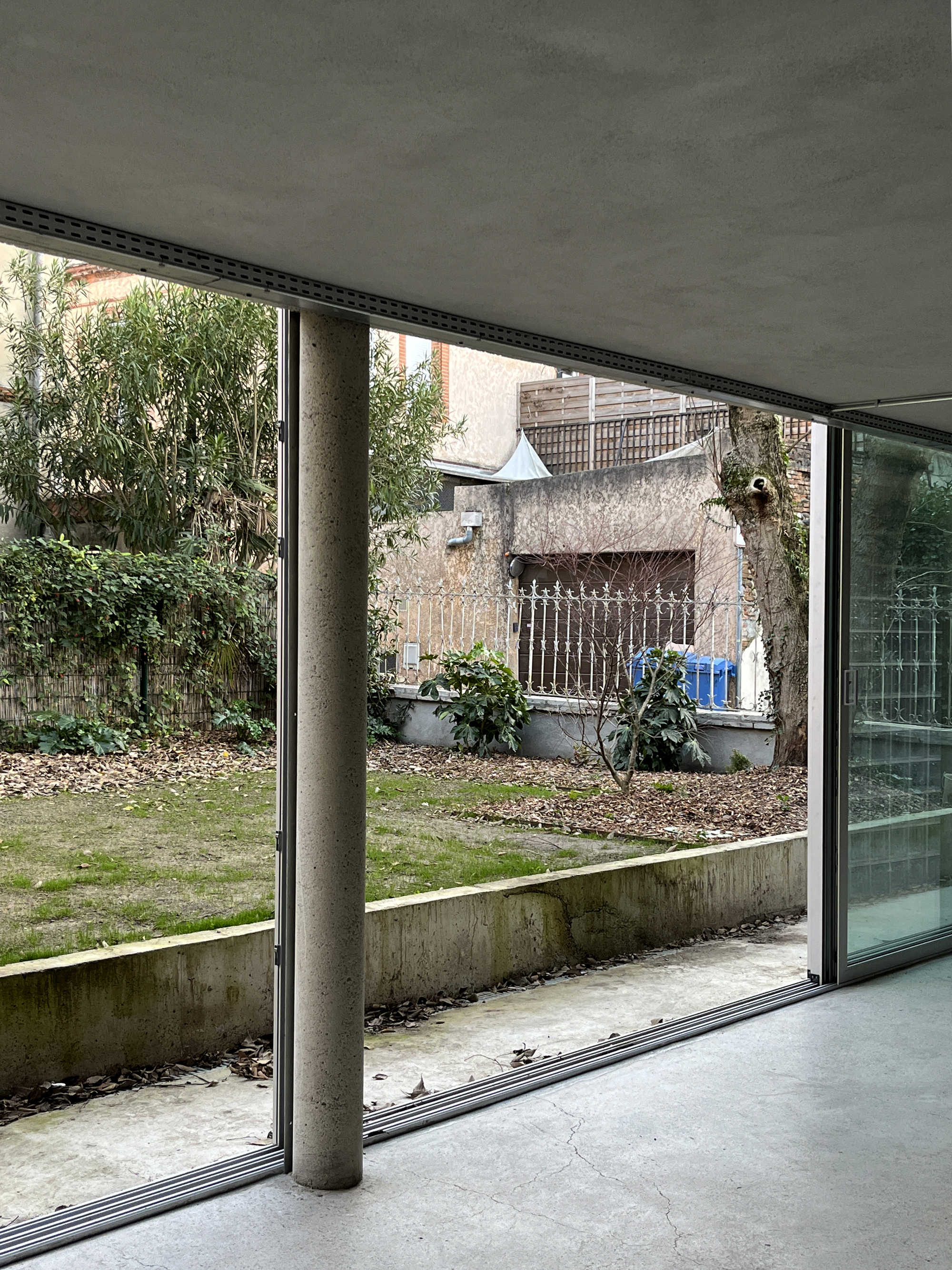 Interior view through floor-to-ceiling glass opening to the garden courtyard with single concrete column