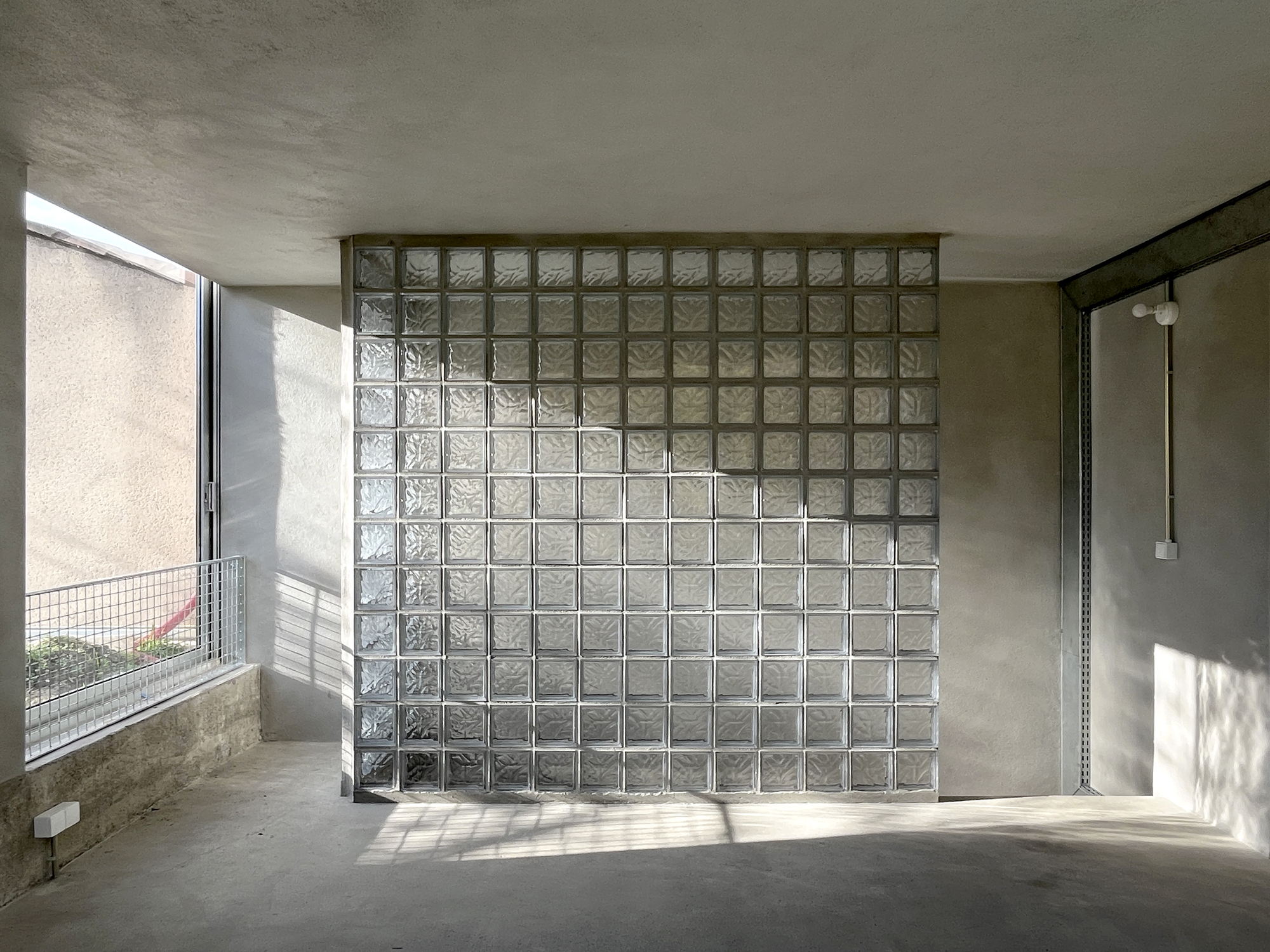 Interior space with freestanding glass block partition wall receiving sharp sunlight from adjacent window opening