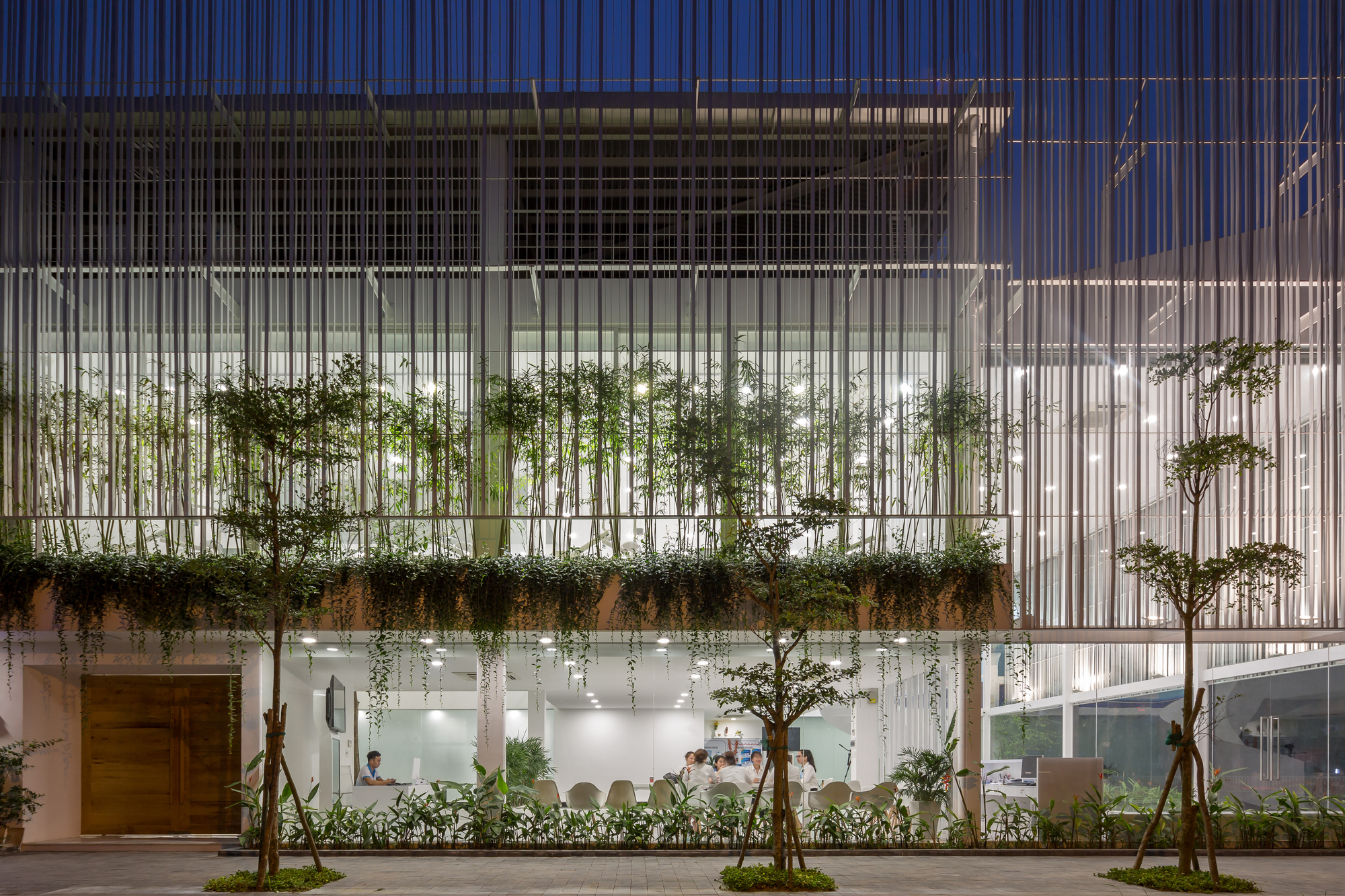 Street facade with vertical white slats screening planted terraces and interior spaces at dusk