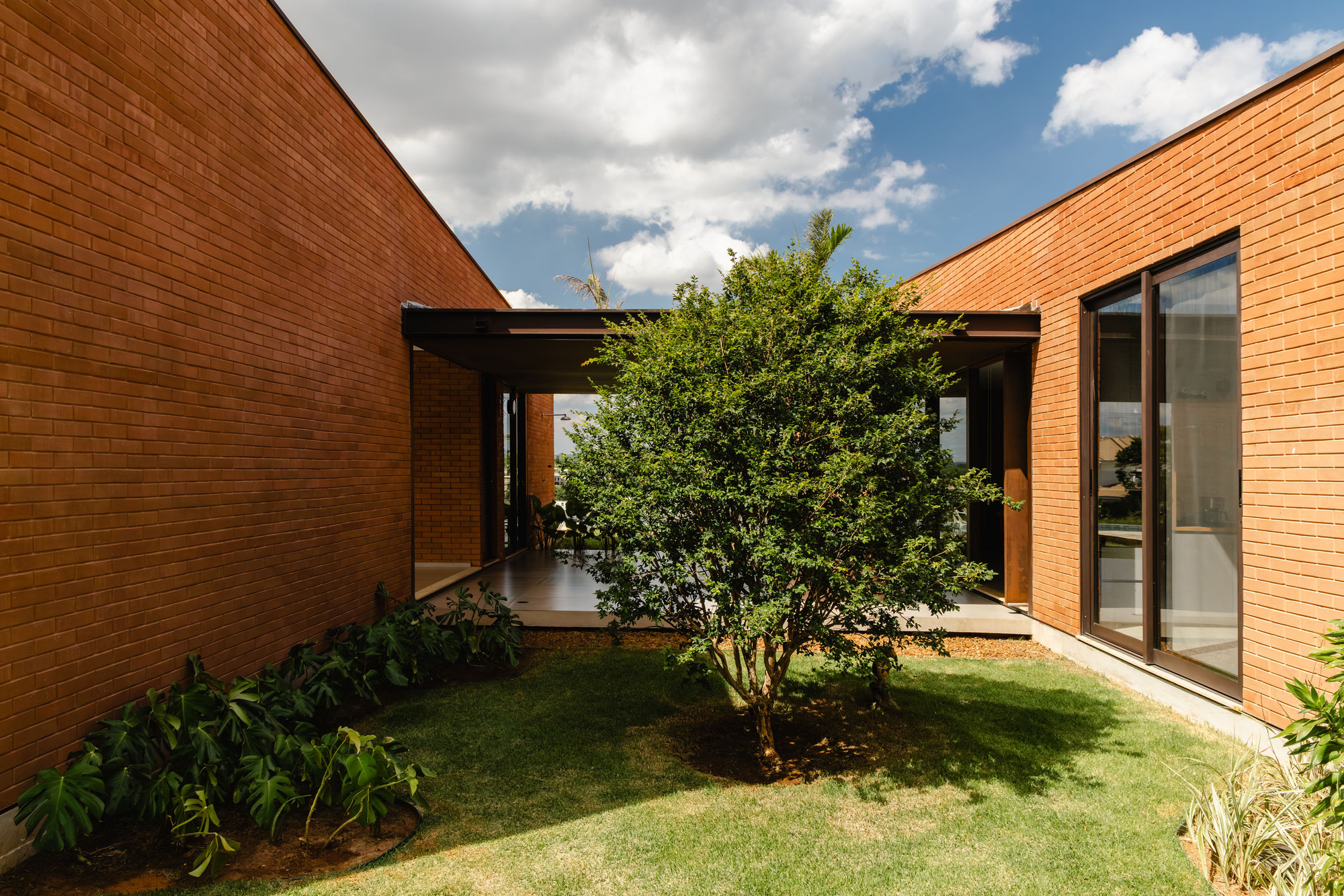 Interior courtyard with tree planted in lawn between brick walls and covered walkway