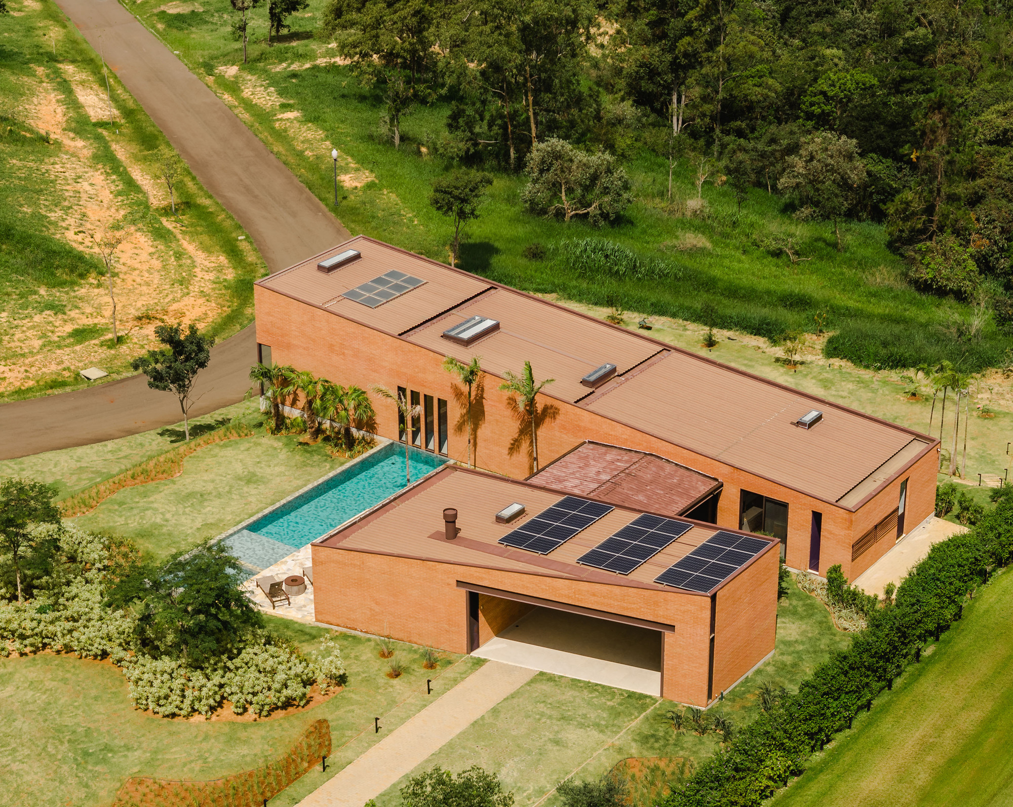 Drone perspective of the L-shaped volumes with photovoltaic arrays and lap pool beside the entry road
