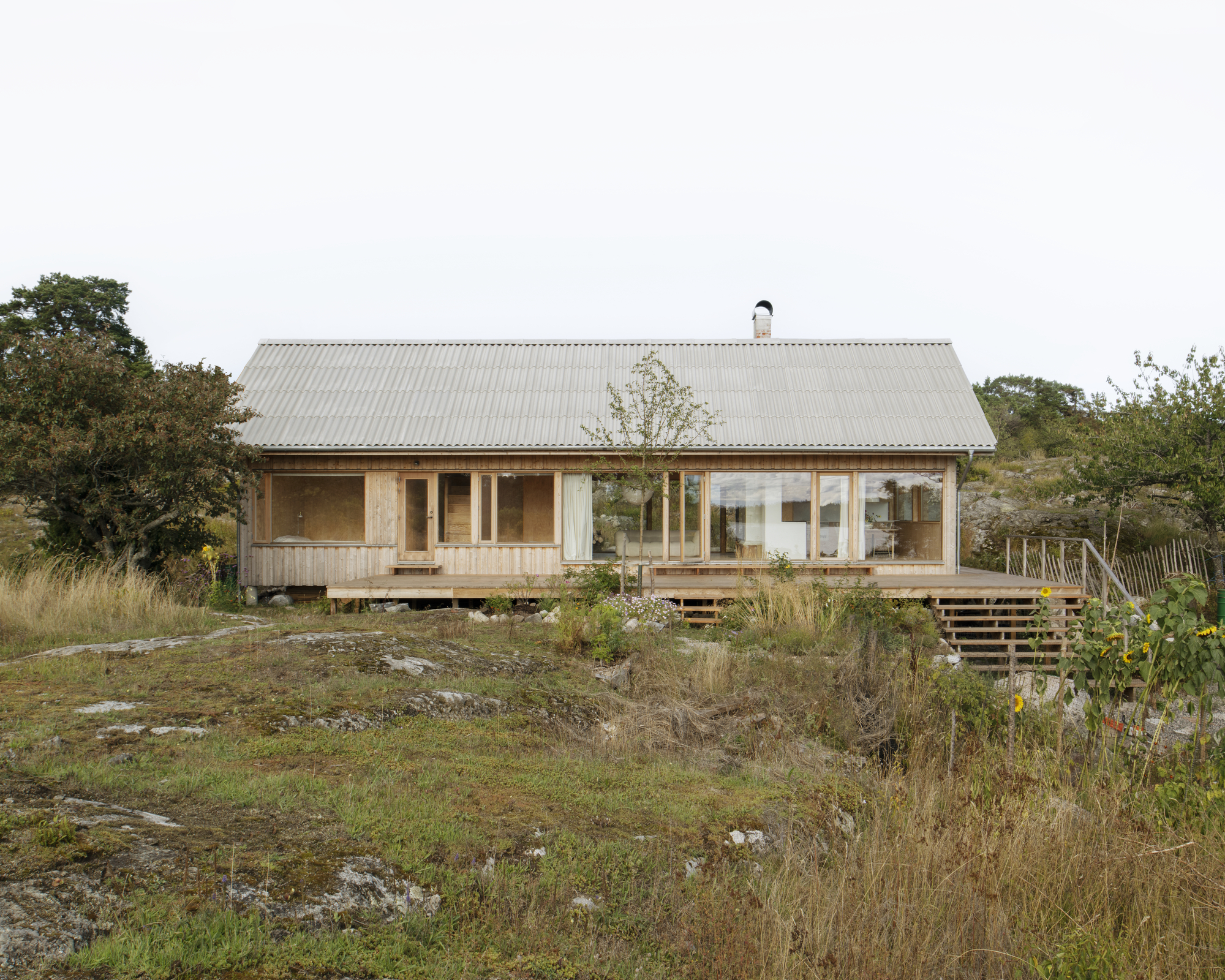 Timber cottage with corrugated metal roof and wraparound deck set among rocky outcrops and grasses