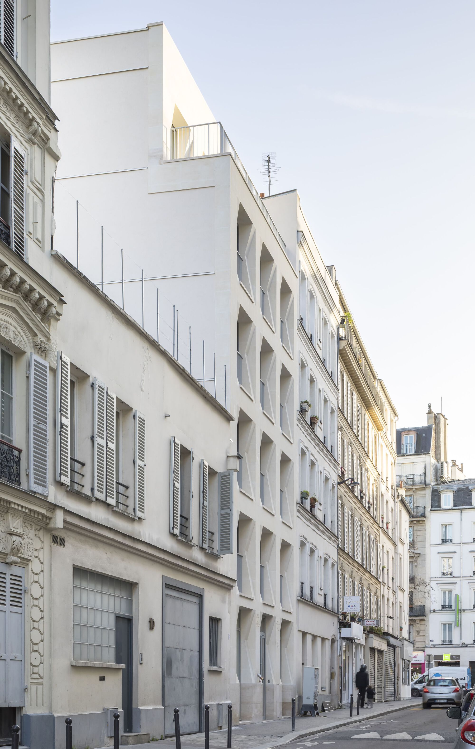 Street view of white residential facade with deep window reveals between ornate heritage buildings