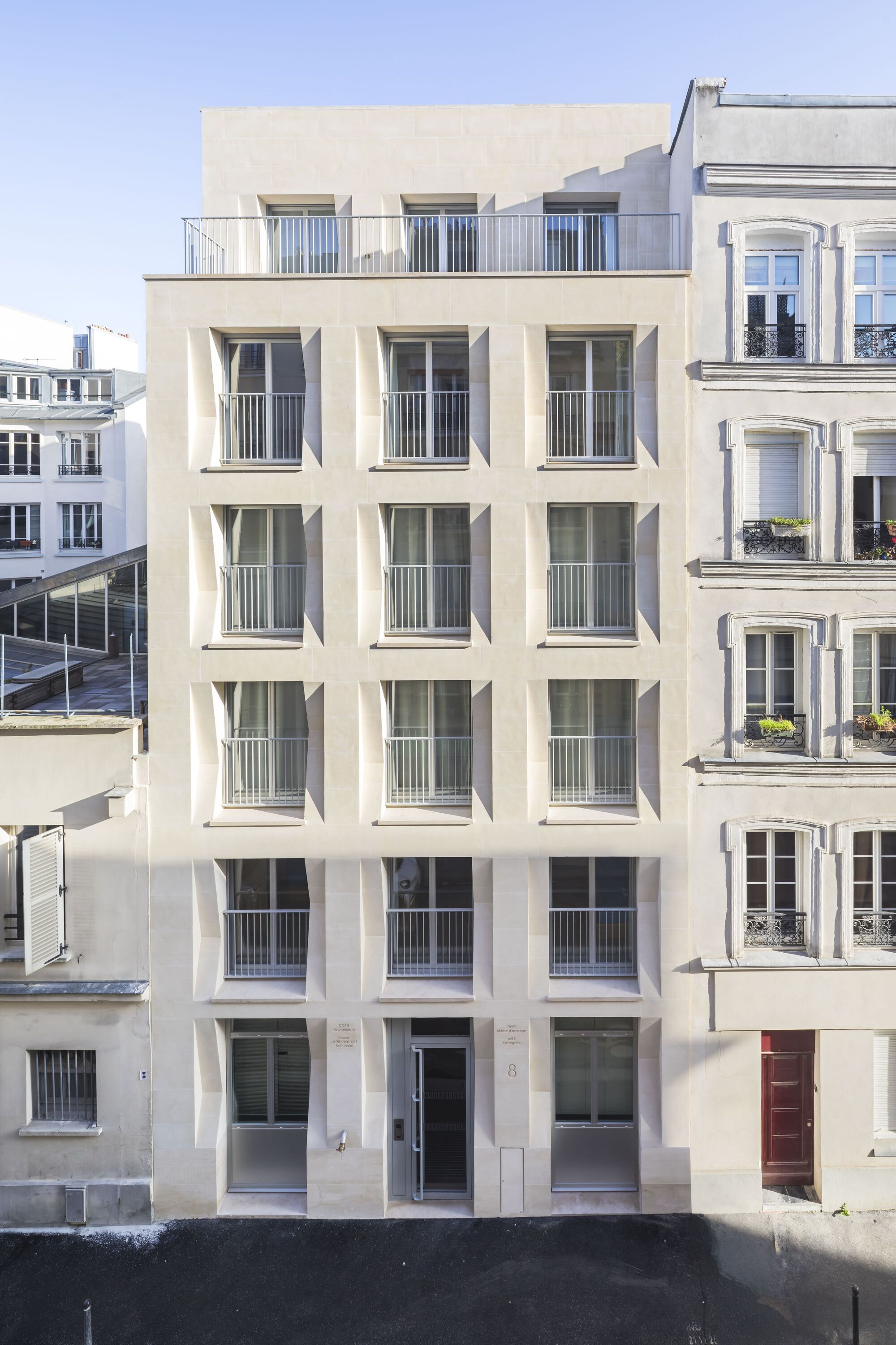 Courtyard elevation with grid of recessed windows and metal balustrades under clear sky