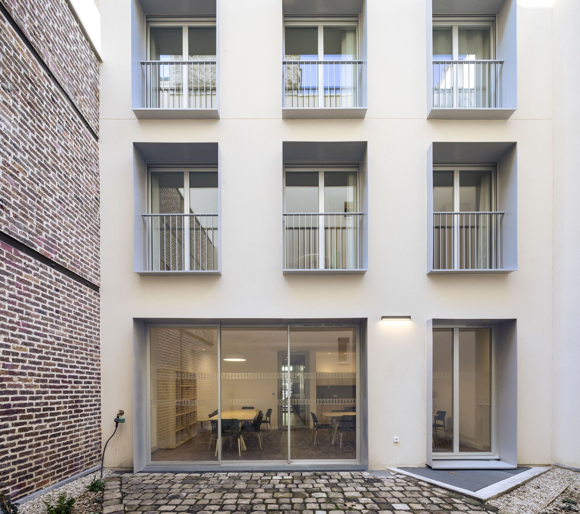 Rear courtyard facade with glazed ground floor opening onto cobblestone paving beside brick wall