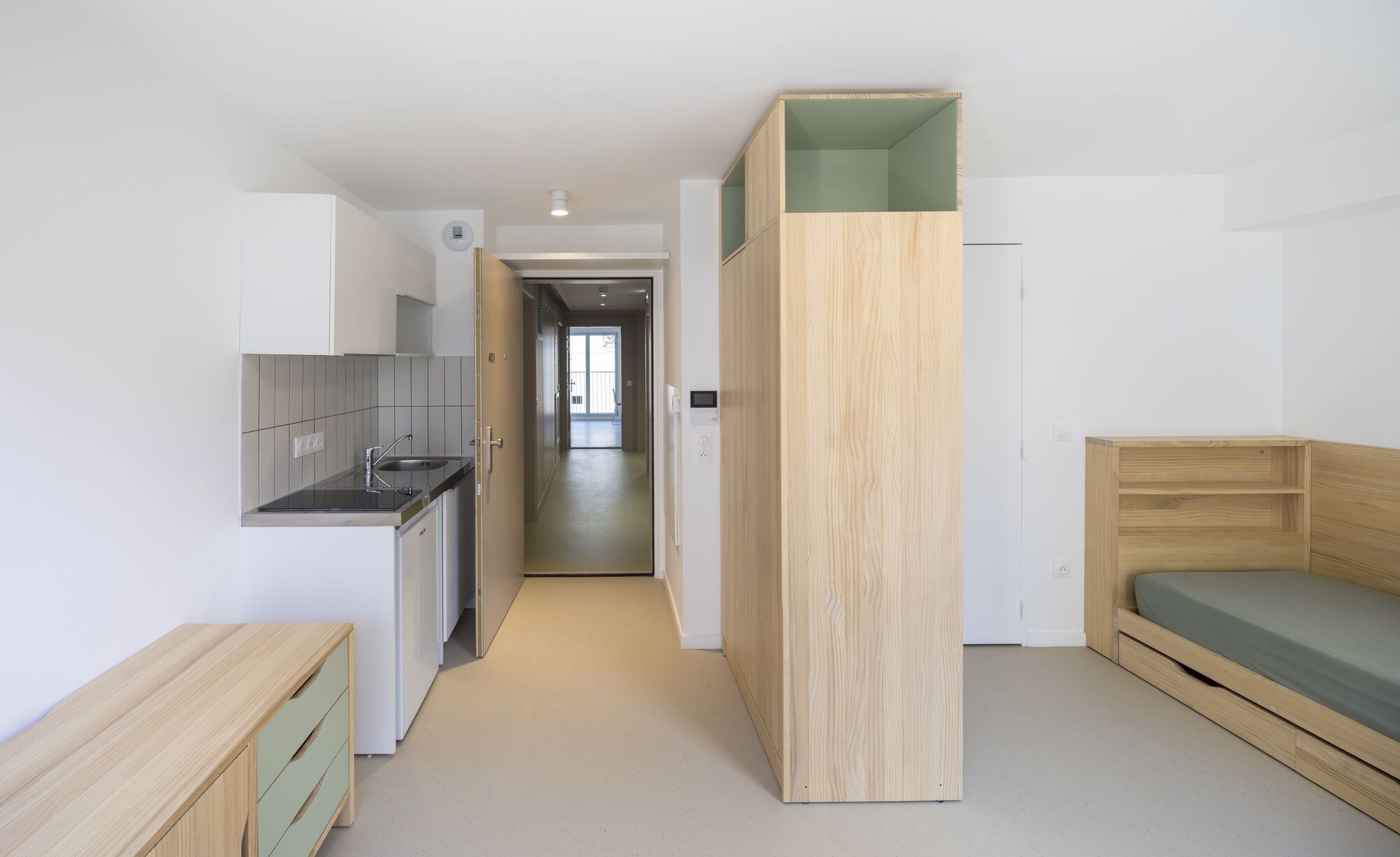 Studio interior with timber wardrobe, bed platform, kitchenette and pale resin flooring
