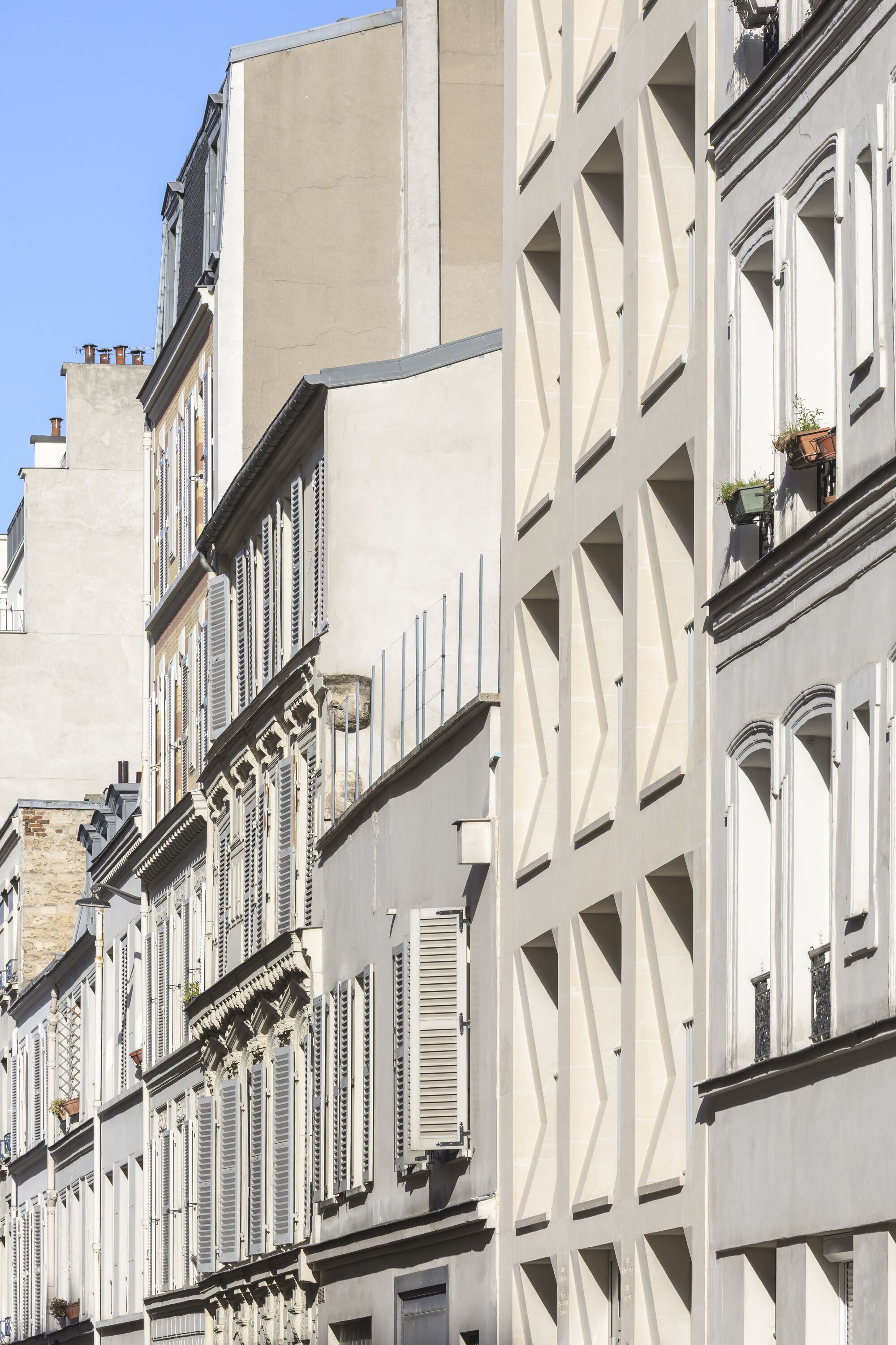 Street view of the faceted white facade alongside neighboring buildings with shuttered windows