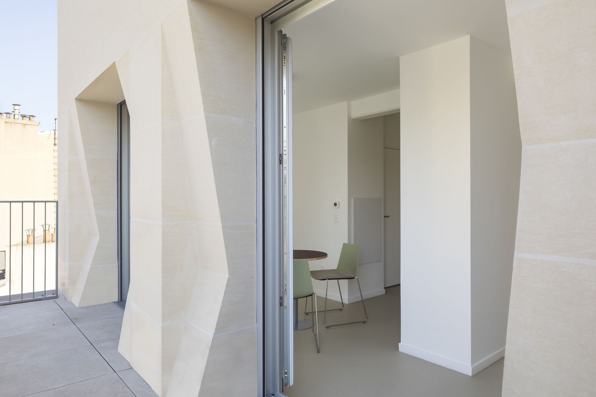 Interior threshold opening from terrace through angular white reveals to dining space beyond