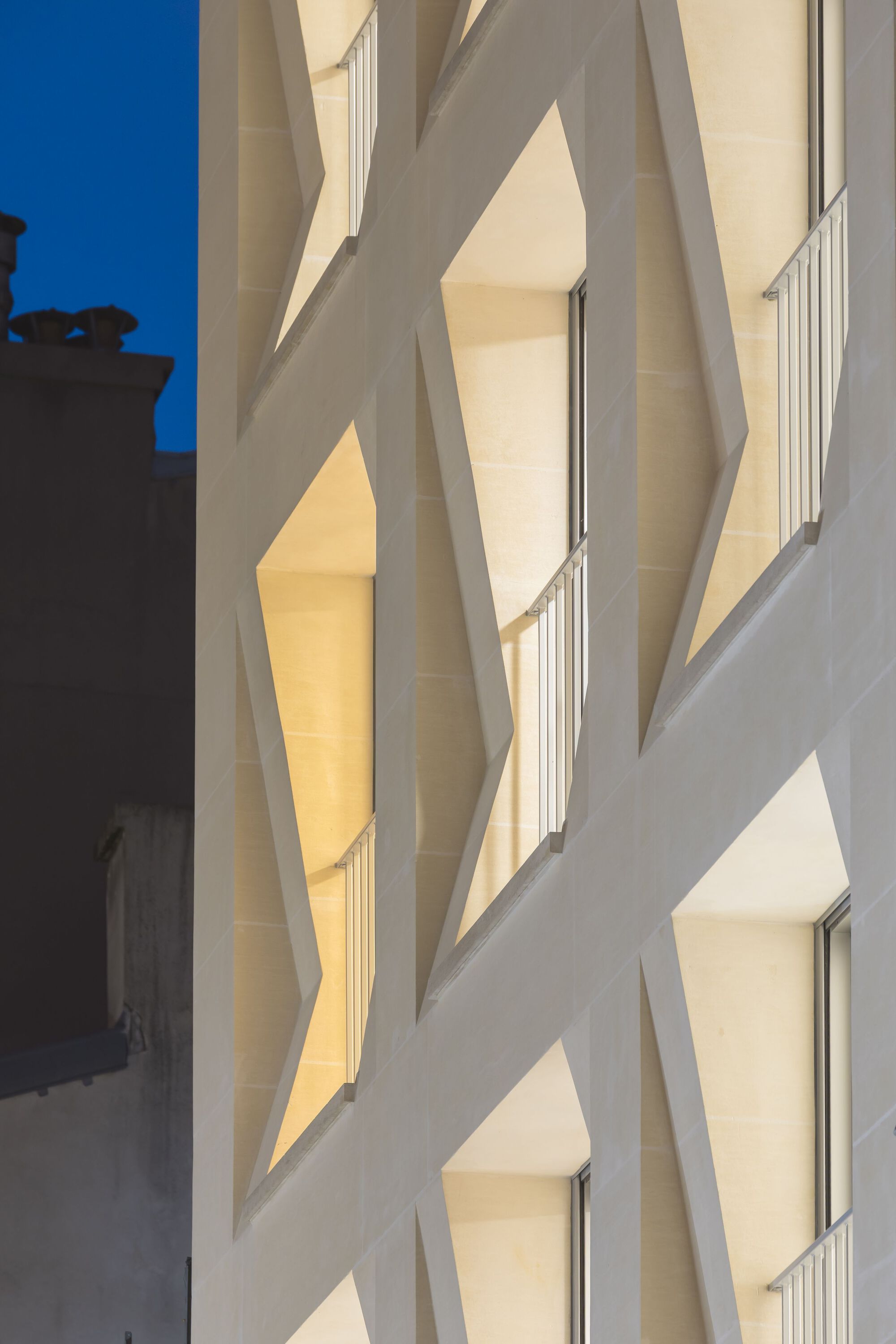 Corner view of the faceted facade illuminated by warm evening light against blue sky