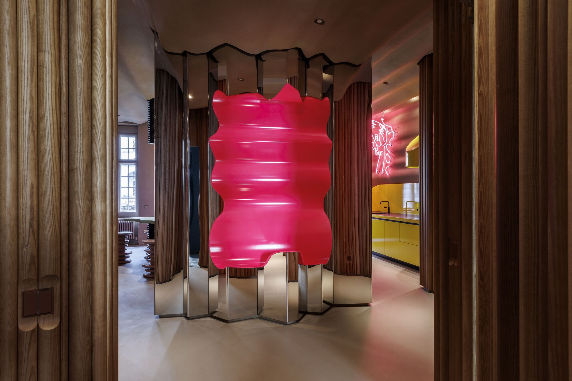 Pink inflatable sculpture on zigzag metal base within timber-clad hallway with views to adjacent rooms