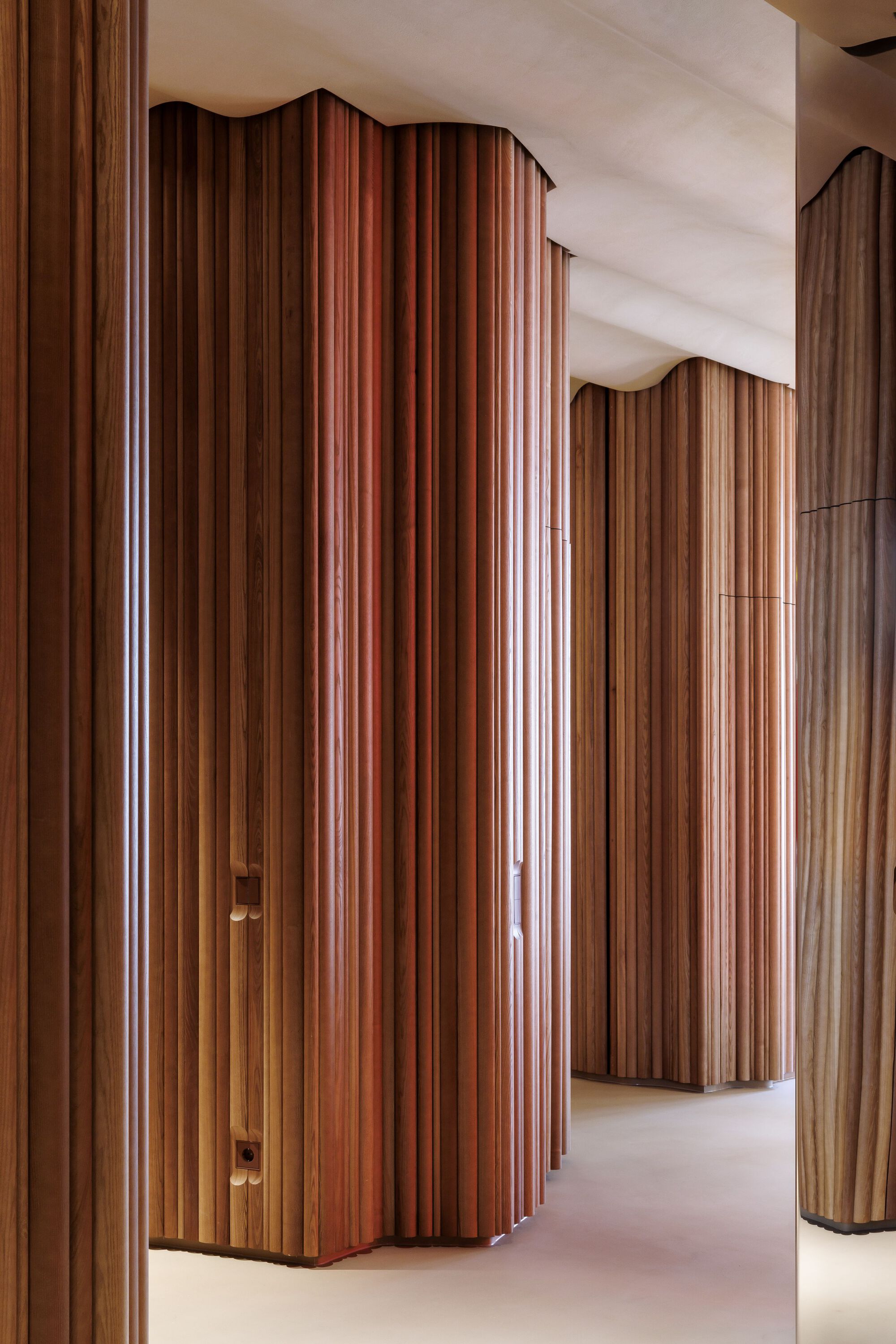 Curved vertical fluted timber wall panels in varying wood tones forming corridor with white ceiling