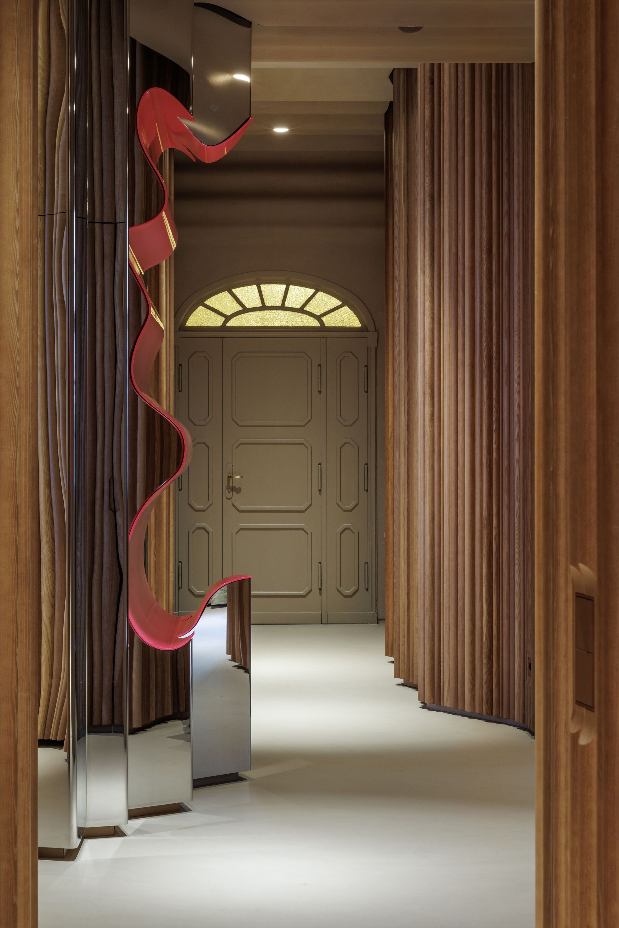 Corridor view toward paneled door with fanlight and red ribbon sculpture along fluted timber walls