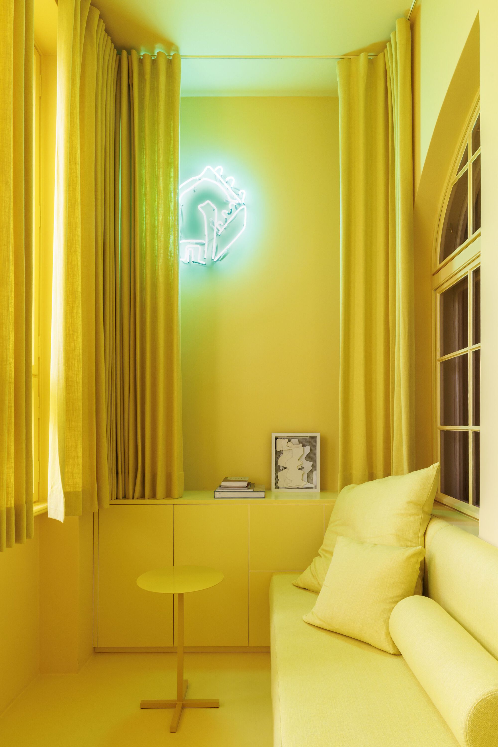 Yellow sitting room with floor-to-ceiling curtains and a neon artwork casting green and yellow light