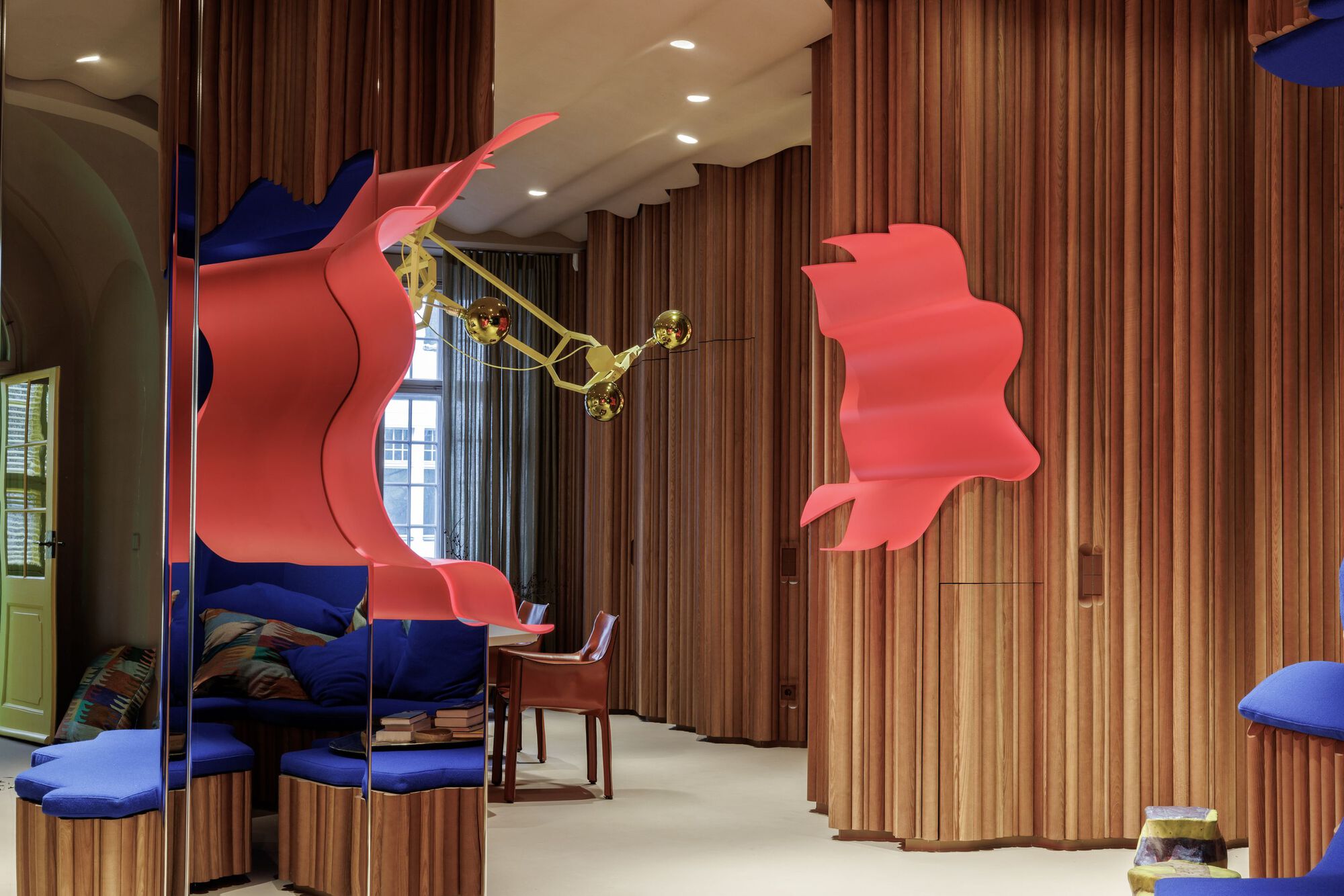 Interior space with curved timber slat partitions and suspended coral-colored sculptural panels