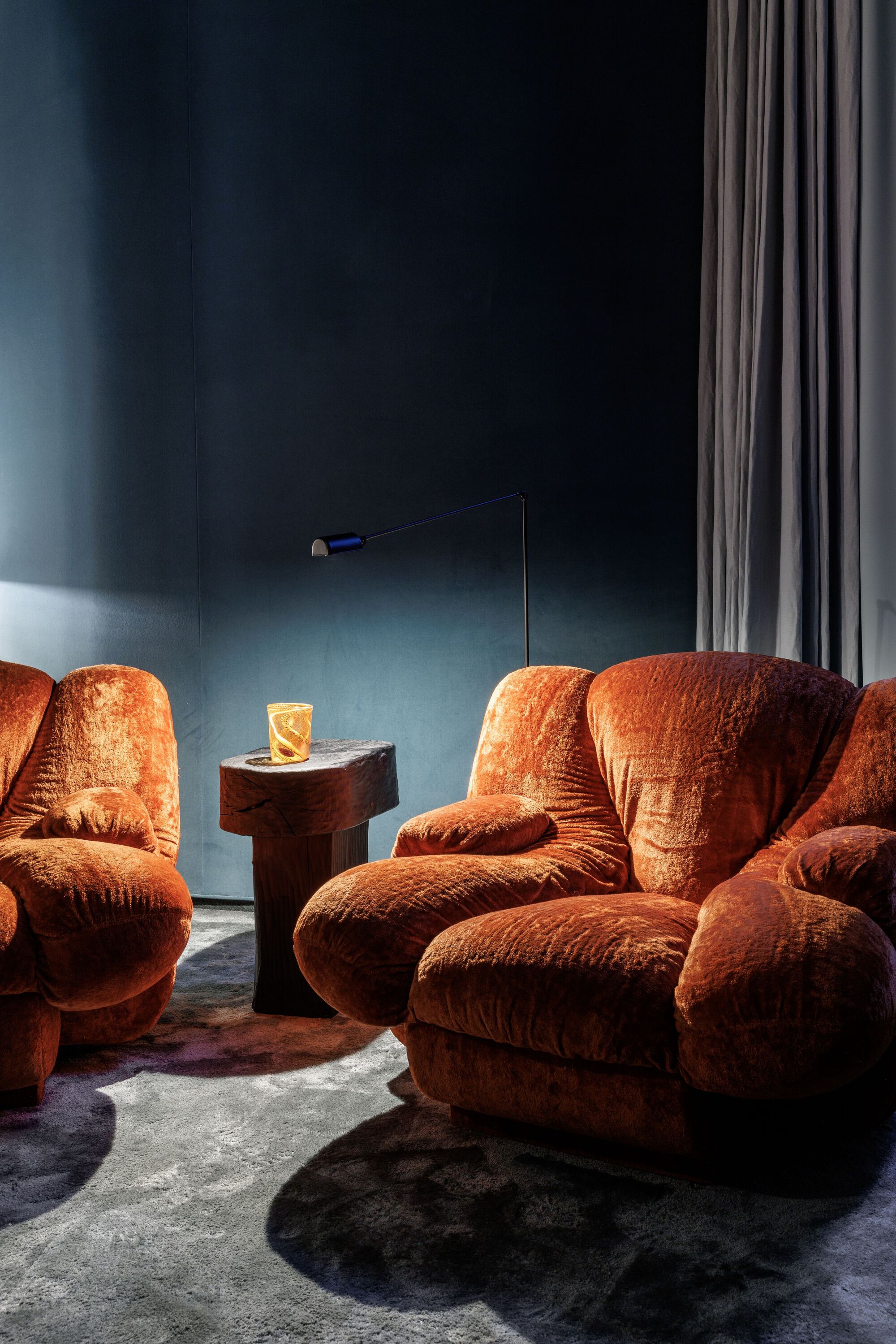Lounge corner with rust-colored velvet chairs grouped around a cylindrical timber side table