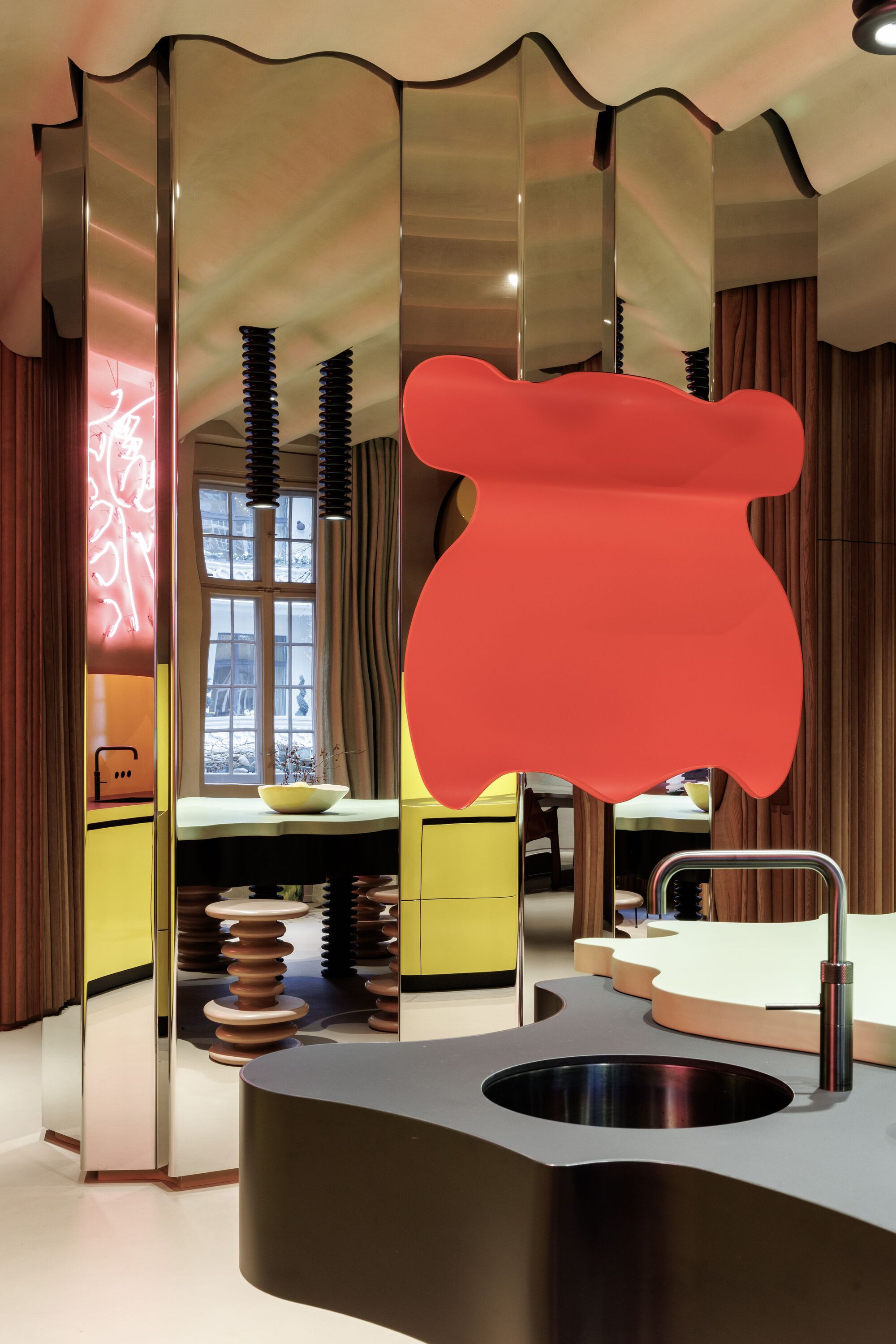 Kitchen island with integrated sink beneath a large coral-colored pendant sculpture and mirrored partition