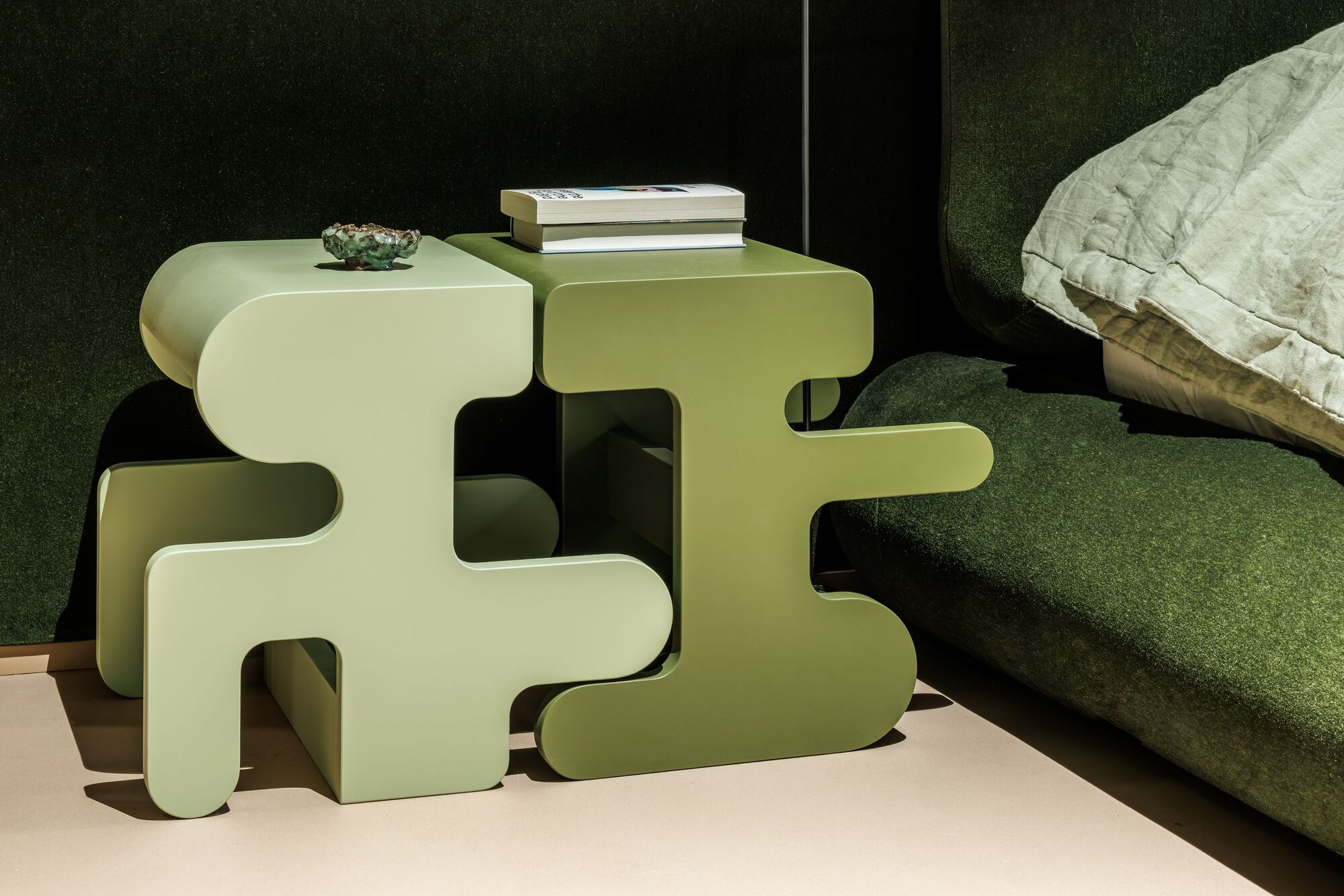 Puzzle-shaped bedside tables in pale green tones next to a dark upholstered headboard
