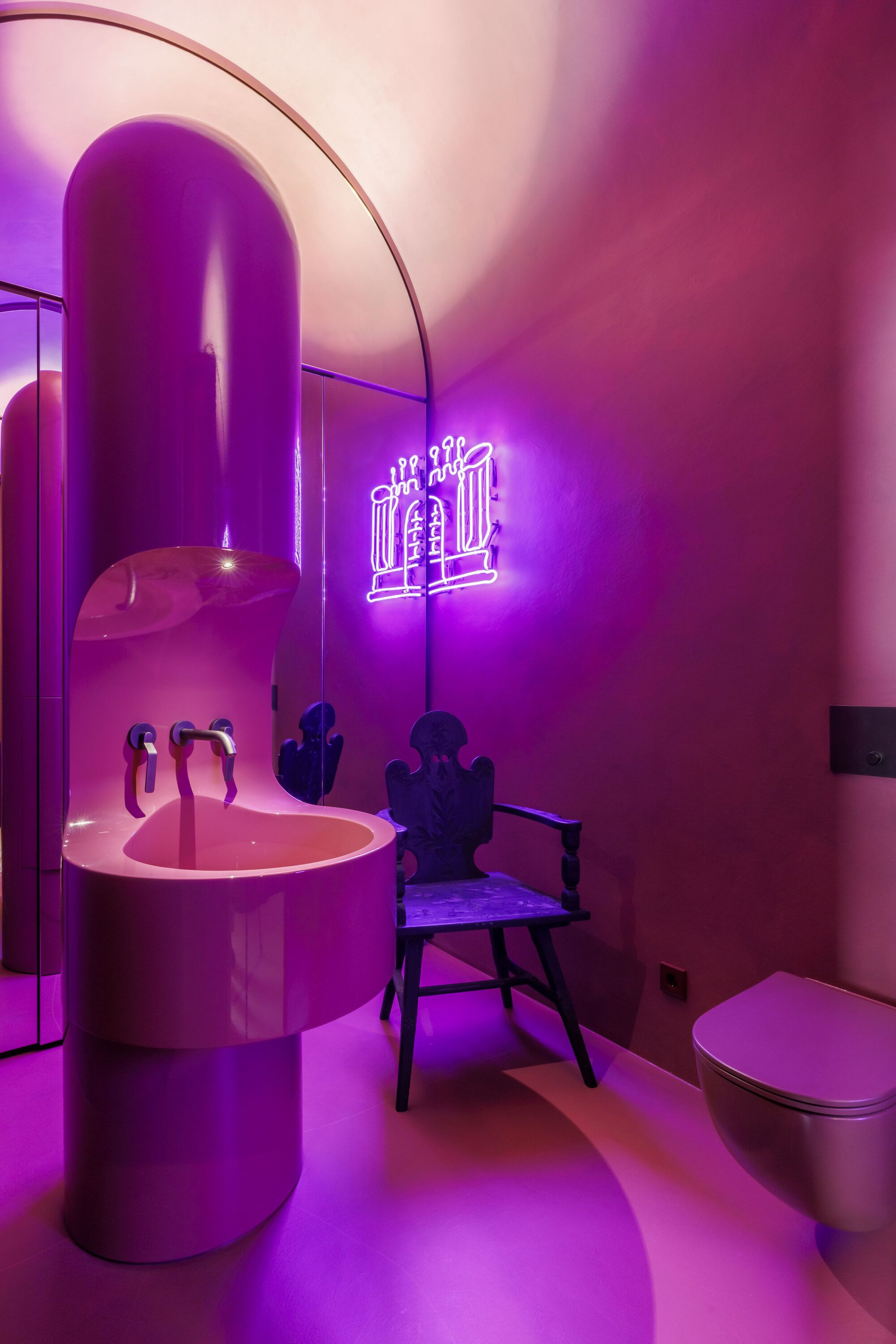 Bathroom with pink cylindrical sink and purple neon lighting illuminating vaulted ceiling and arched doorway