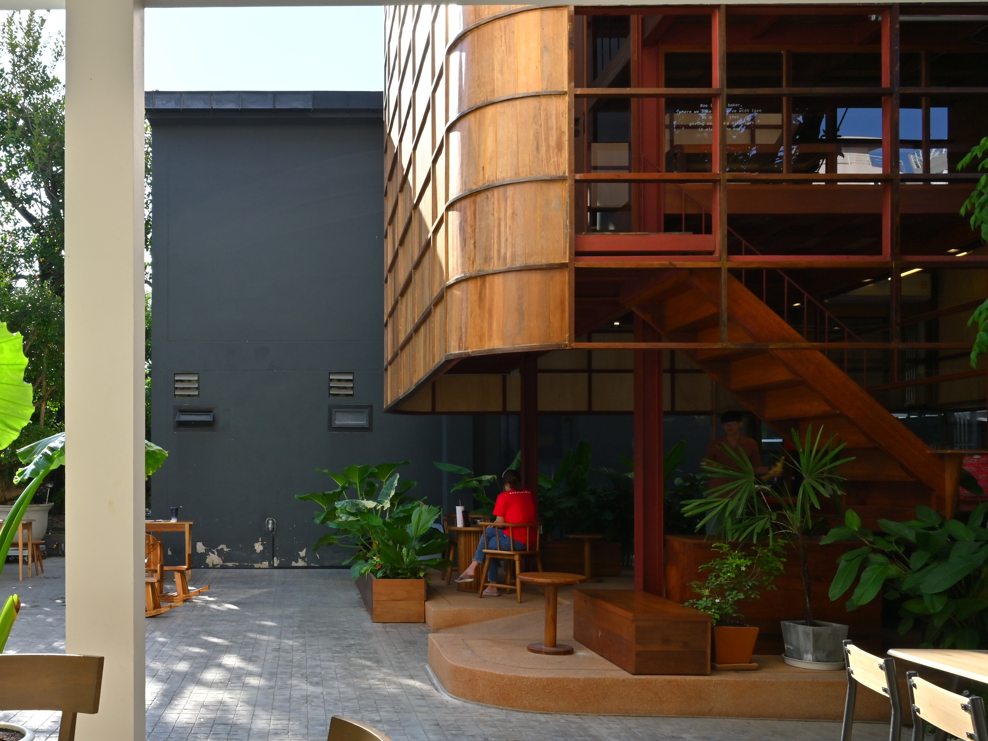 Curved timber stairs wrapping around planted courtyard terrace framed by white columns and tropical foliage
