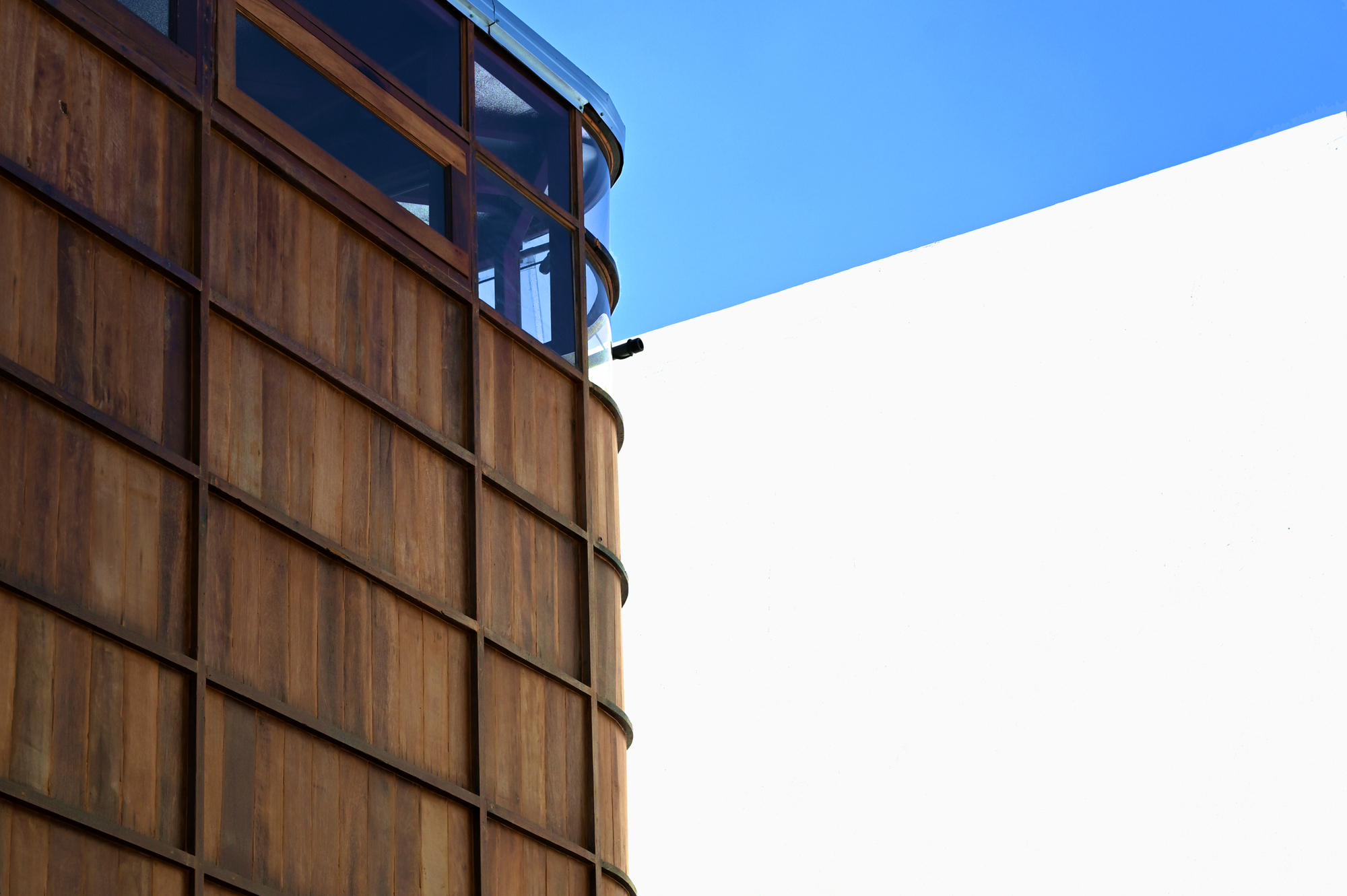 Junction of the cylindrical timber-clad volume with glazed upper level and white rendered wall