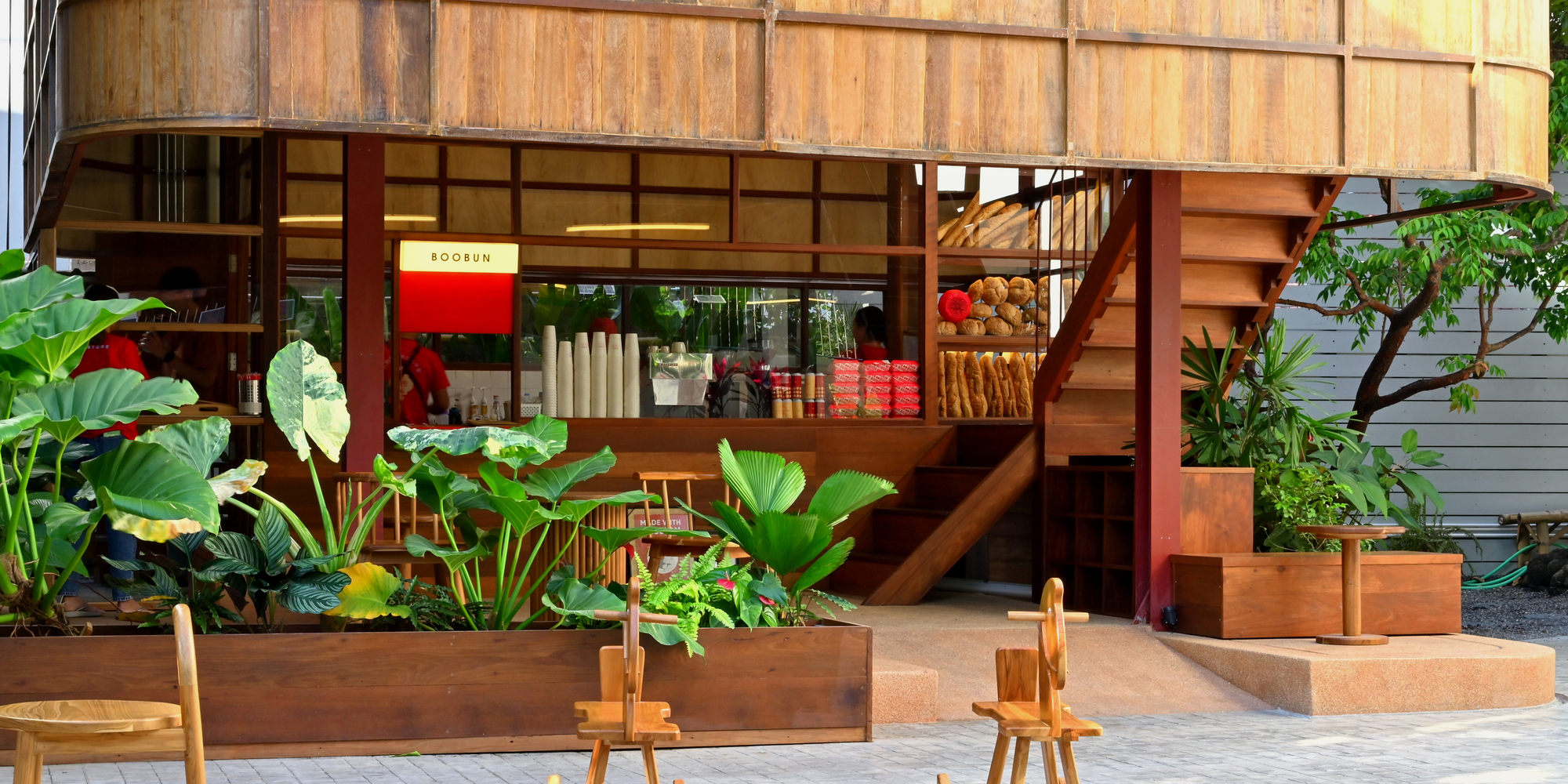 Glazed shopfront beneath the curved timber volume with planted beds and timber seating in foreground