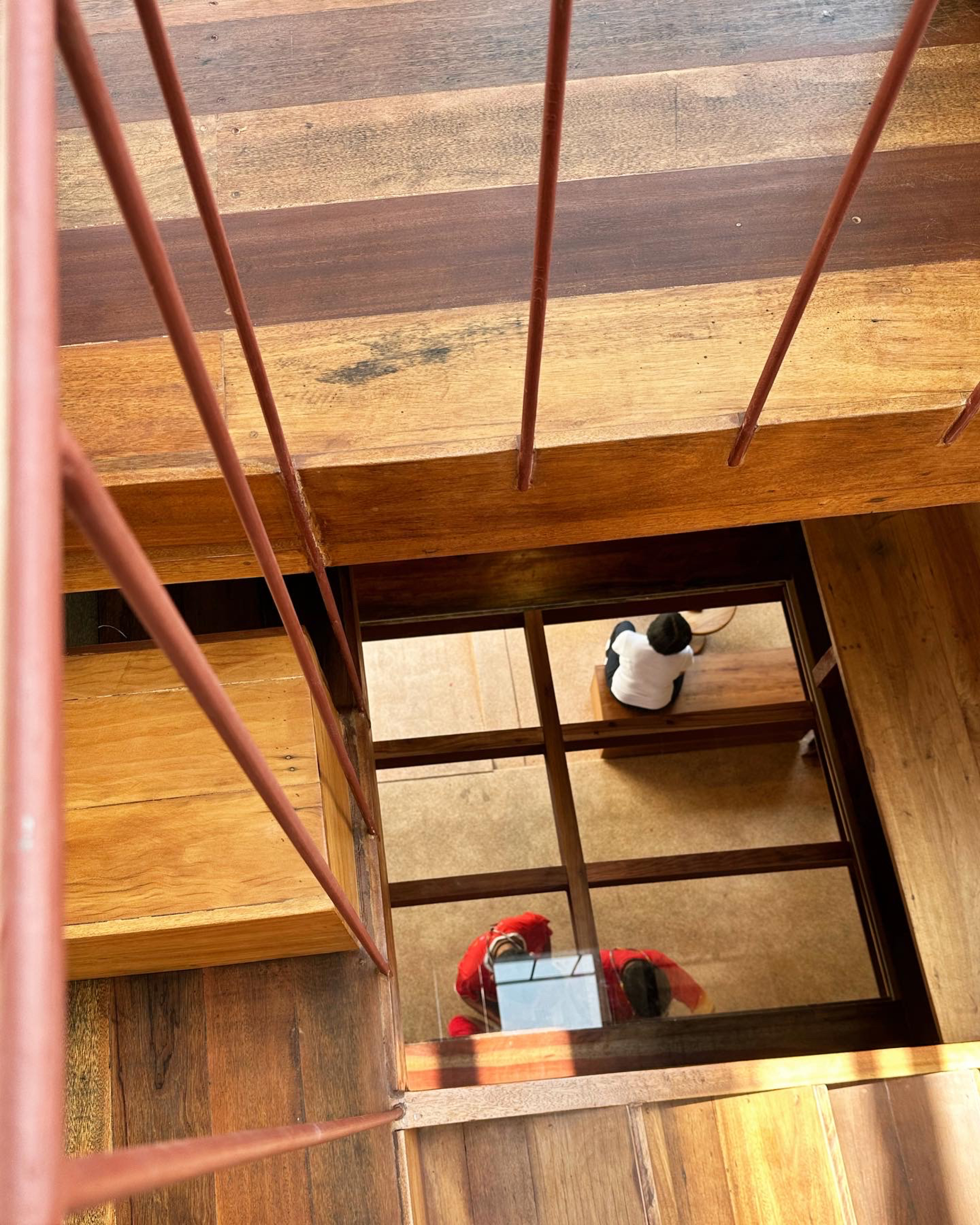 Looking down through floor opening with steel railing as two people sit at table below