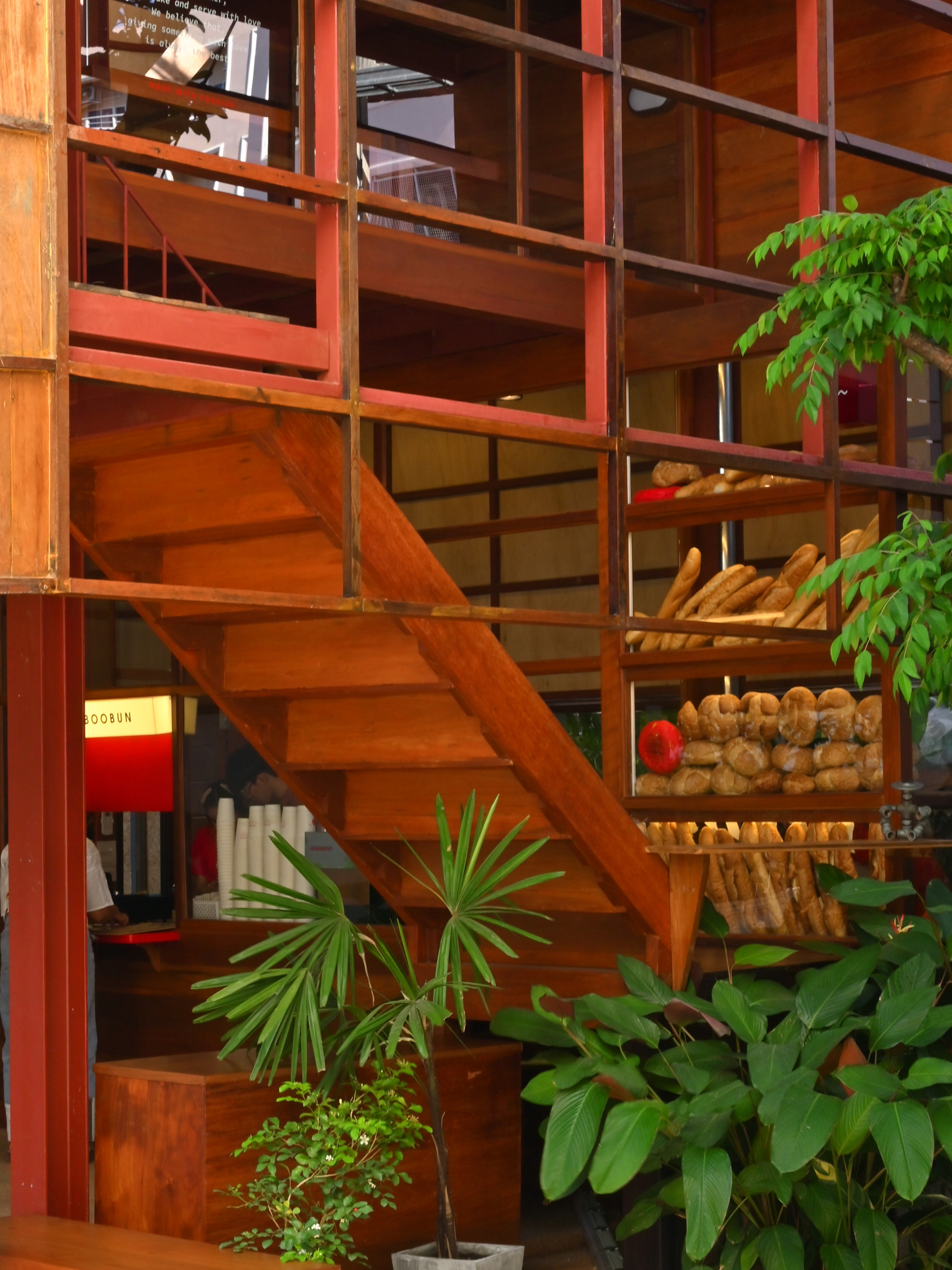 Red steel grid facade framing timber staircase and interior shelving with potted plants